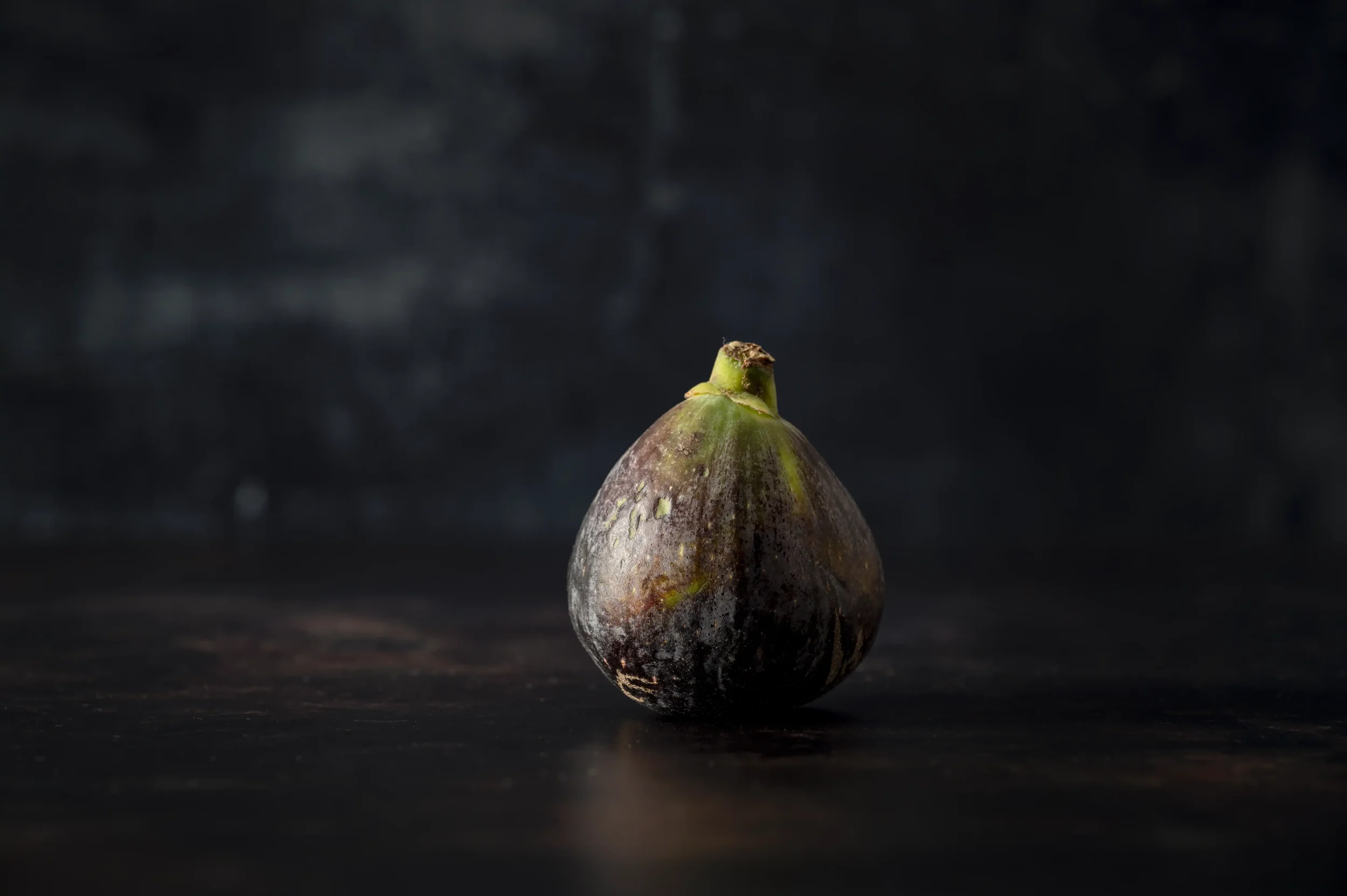 Colour photograph of a single fig on a dark background