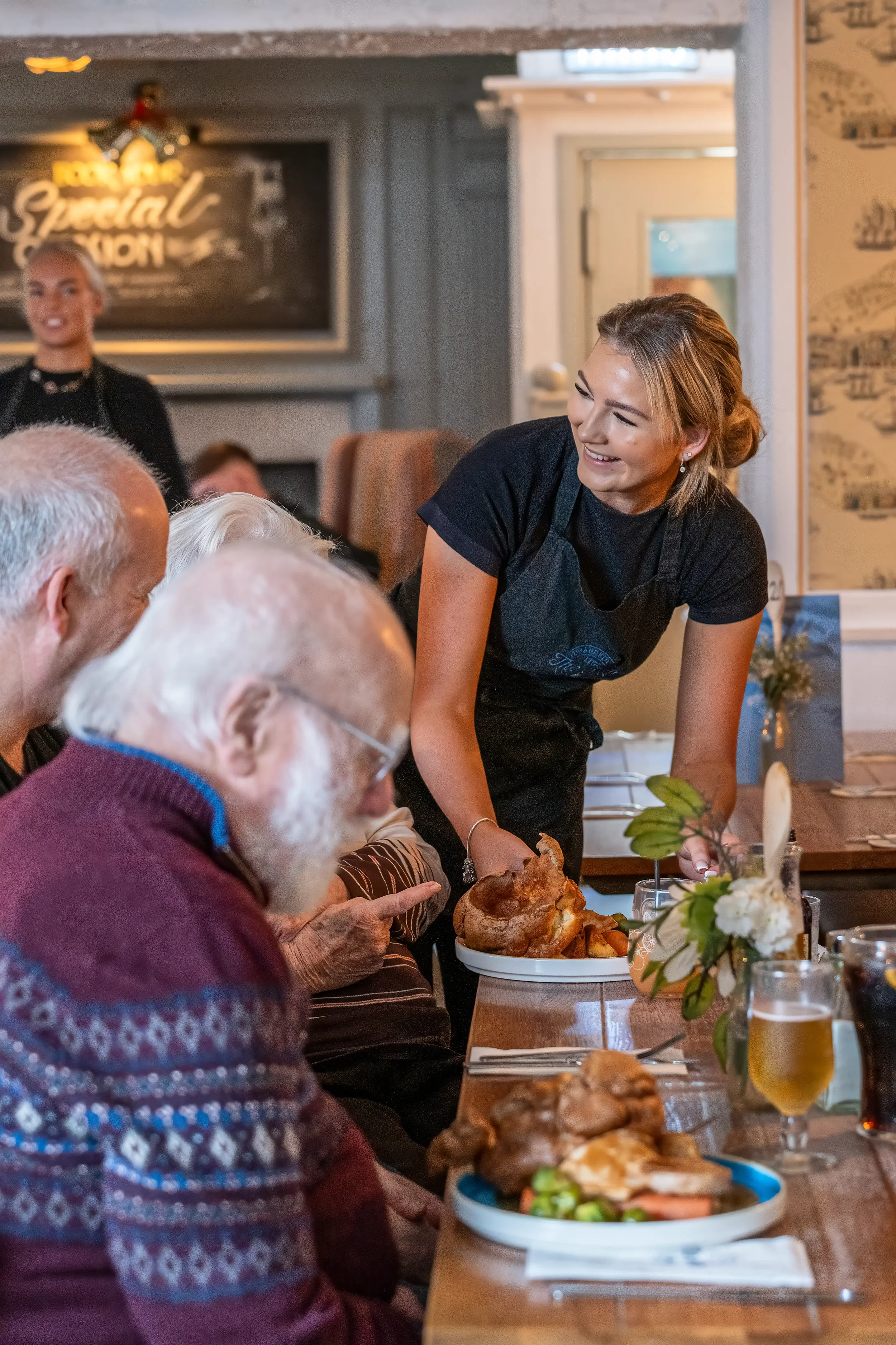 Colour photograph of a smiling waitress serving Sunday lunch to a customer in a warm an inviting country pub