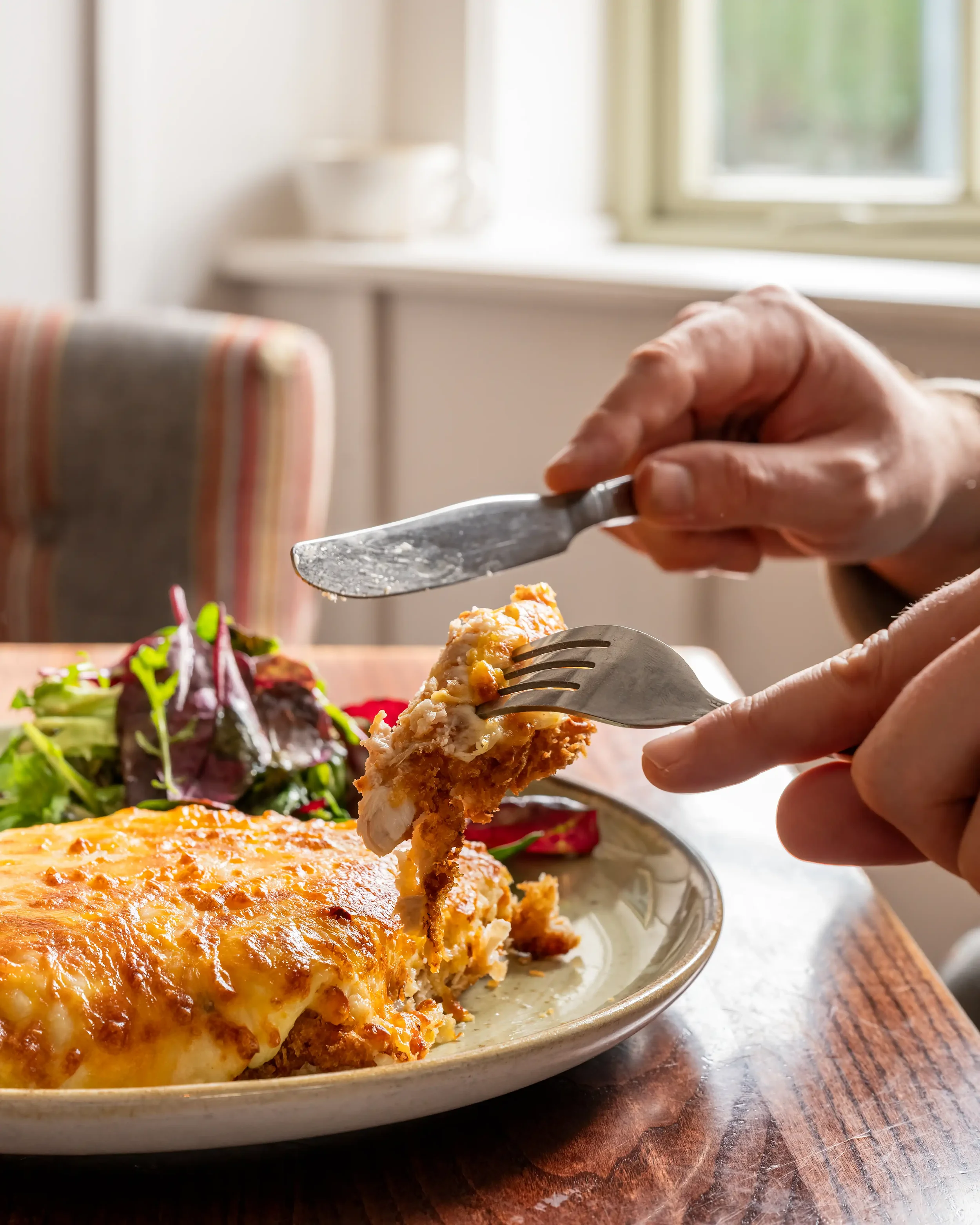 Colour photograph of a person eating a meal next to a window in a country pub