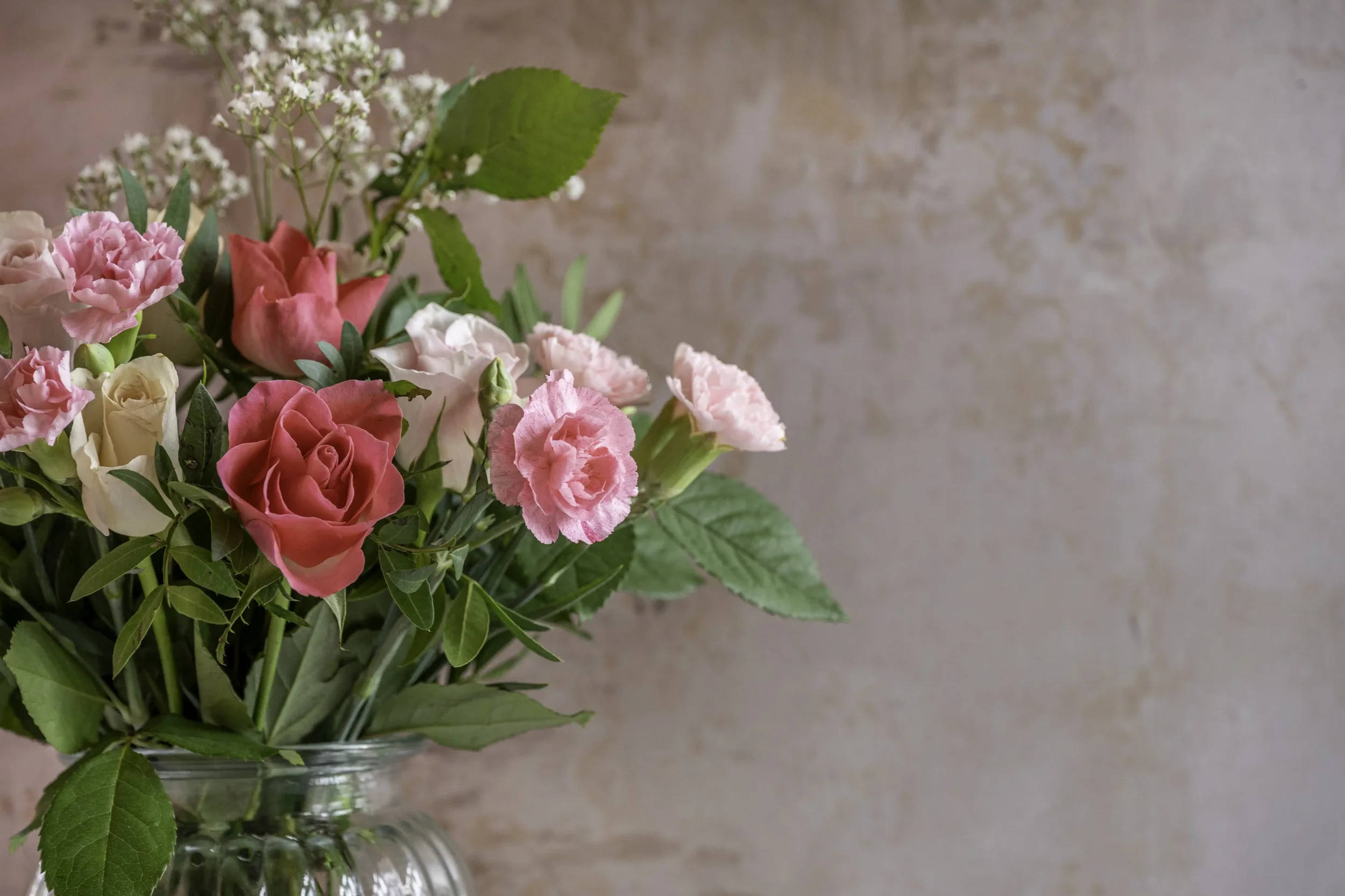 Photograph of some pink and red flowers in a glass vase against a dusky pink background