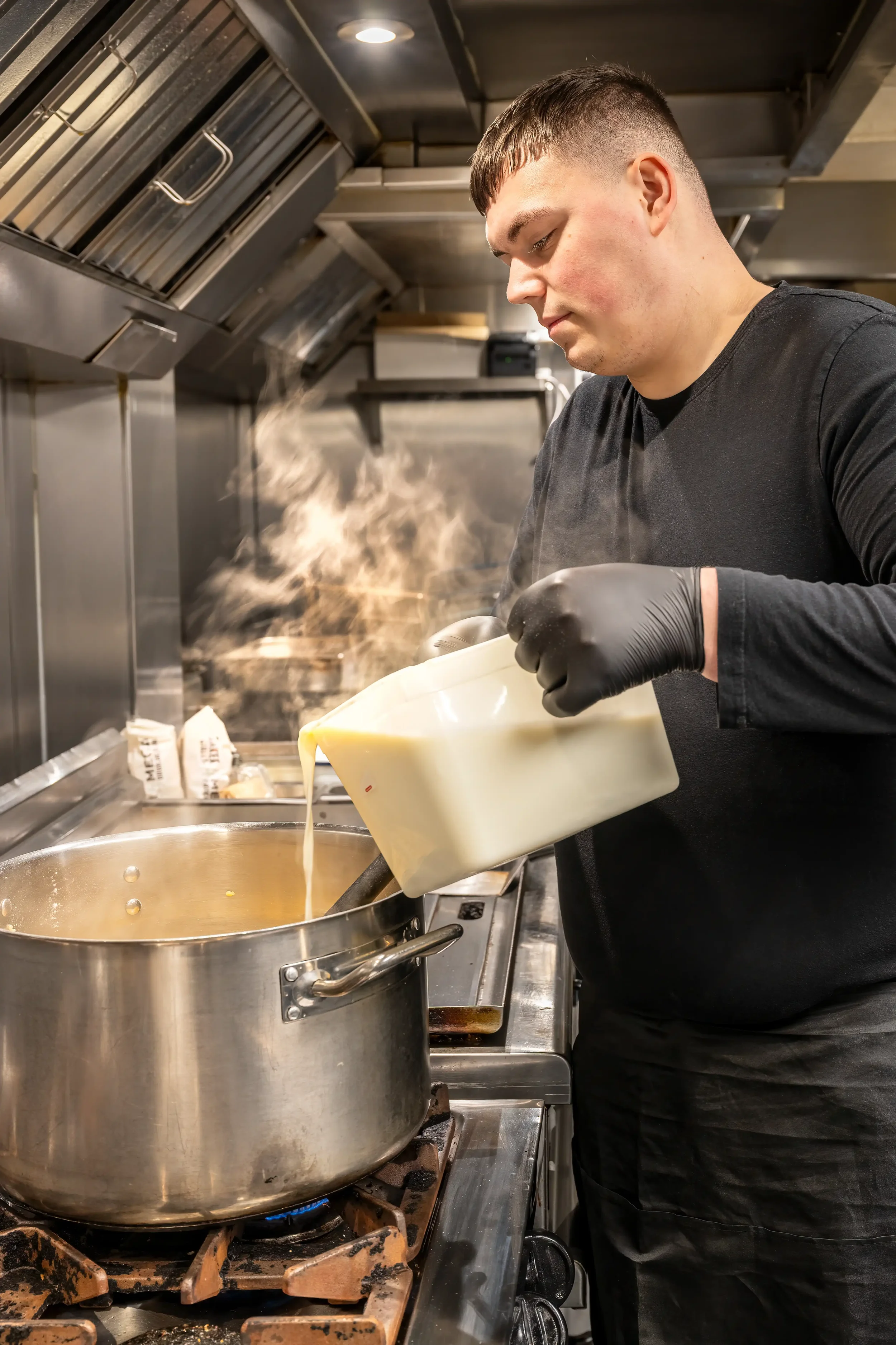 Colour photograph of a cook working in a commercial kitchen preparing a batch of bechamel sauce