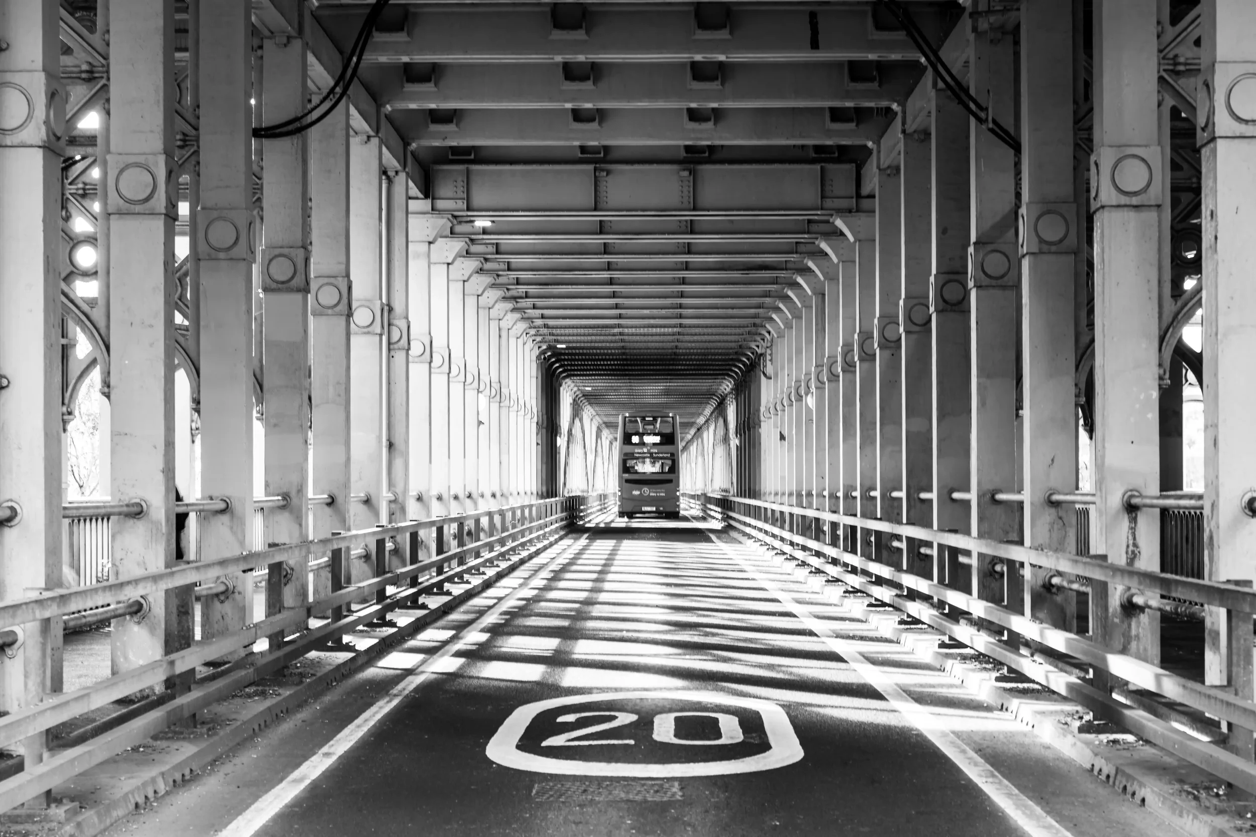 Black and white photograph of a bus travelling away from us across the High-Level Bridge in Newcastle upon Tyne