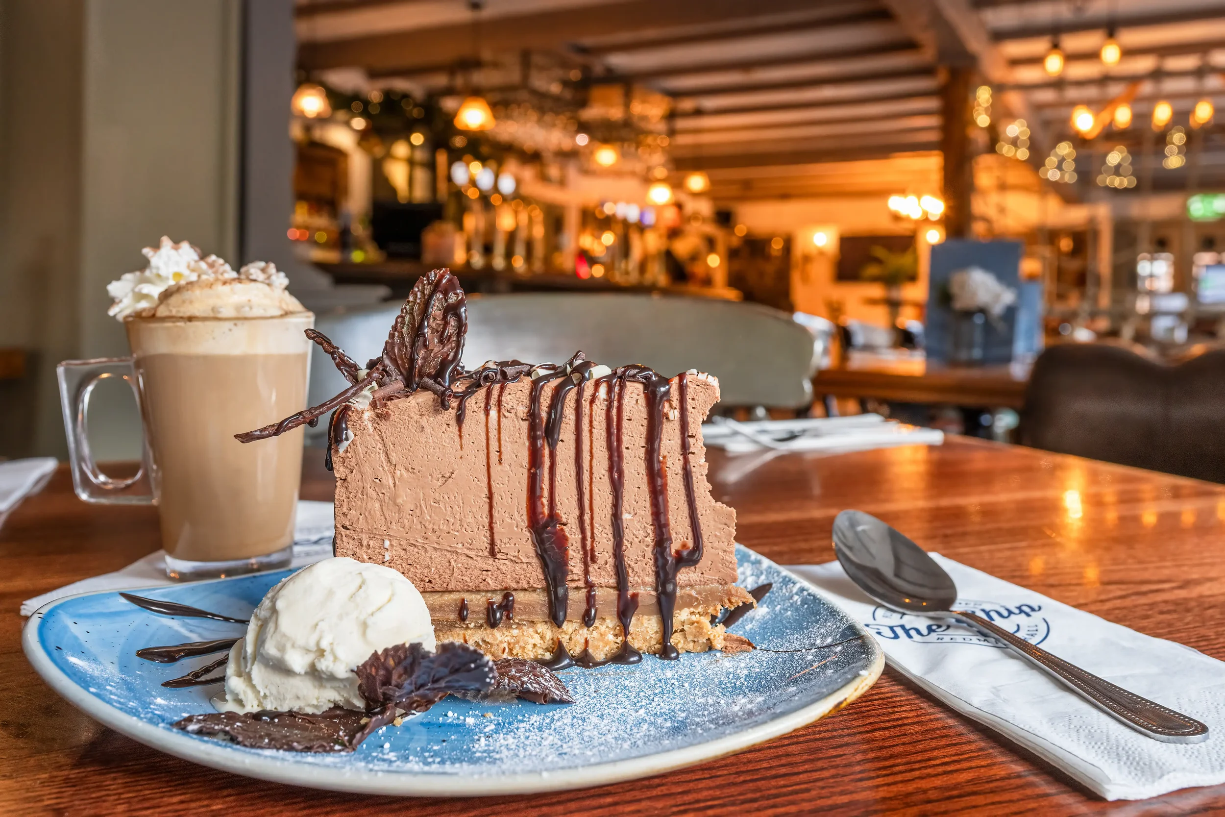 Colour photograph of a large slice of chocolate cheesecake and a cafe latte in a country pub