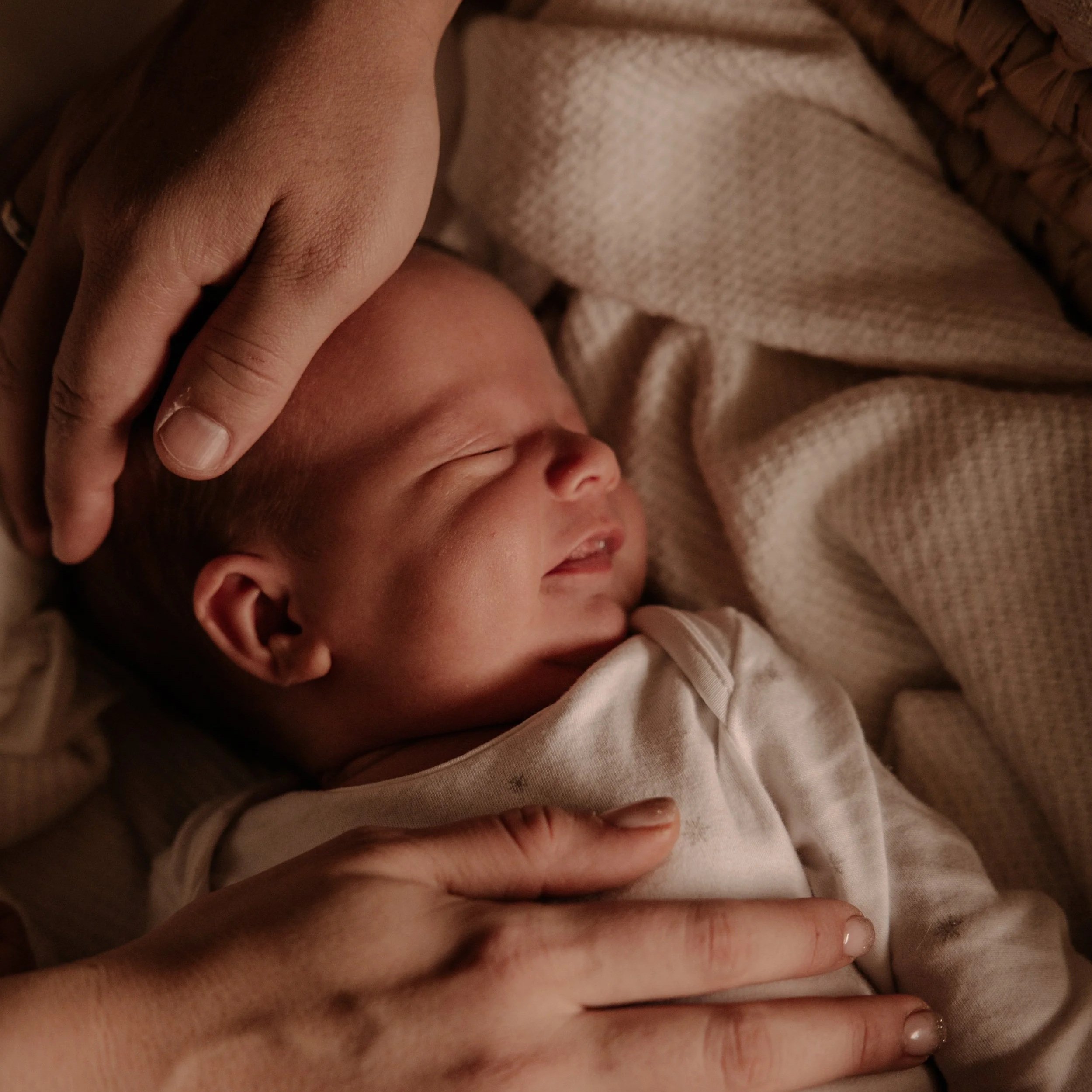 Friedlich schlafendes Baby in einer Wiege mit den Händen der Eltern.