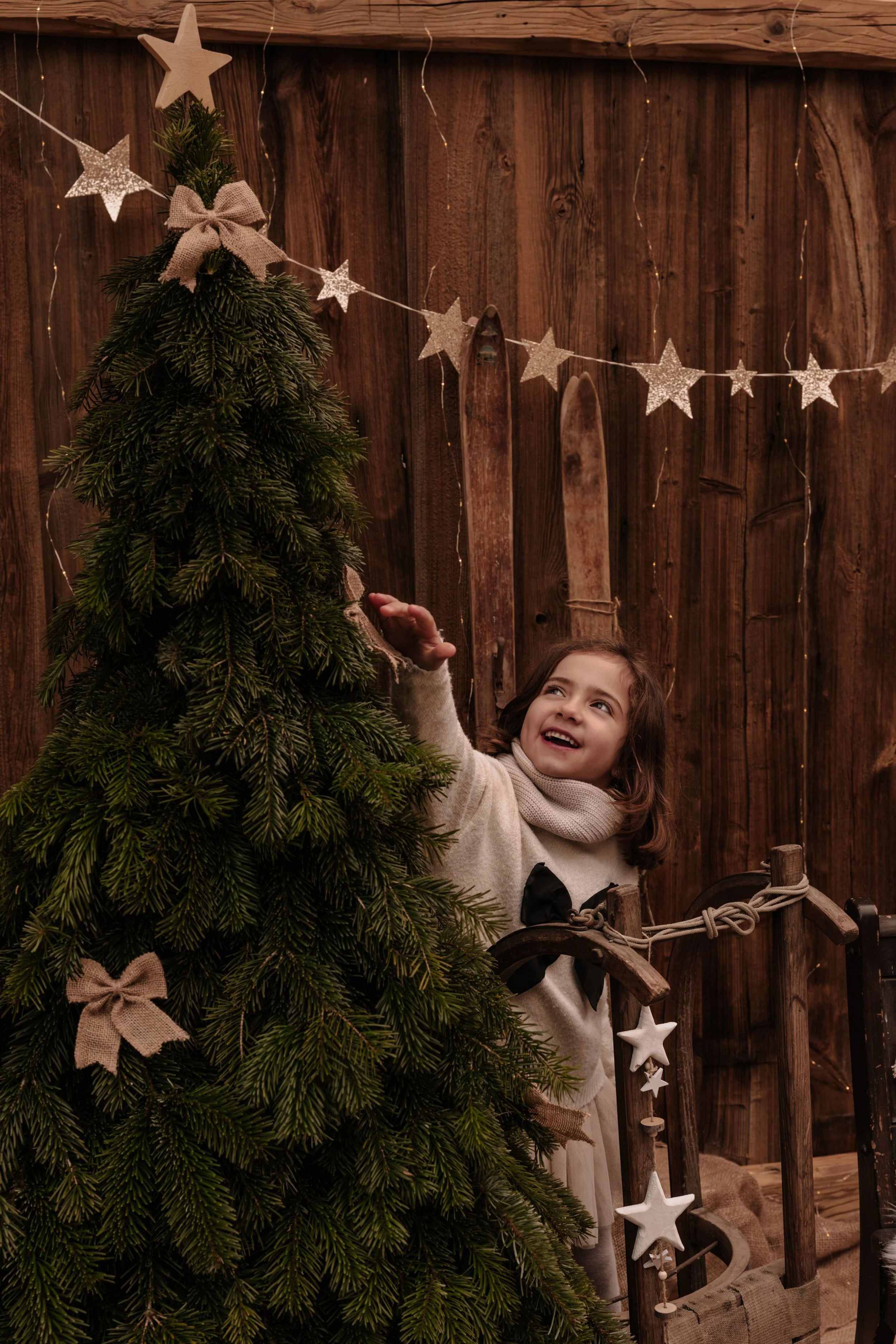 Ein lachendes Mädchen in einem winterlichen Raum, der mit Dekorationen wie einem Weihnachtsbaum, Sternen und Schleifen geschmückt ist.