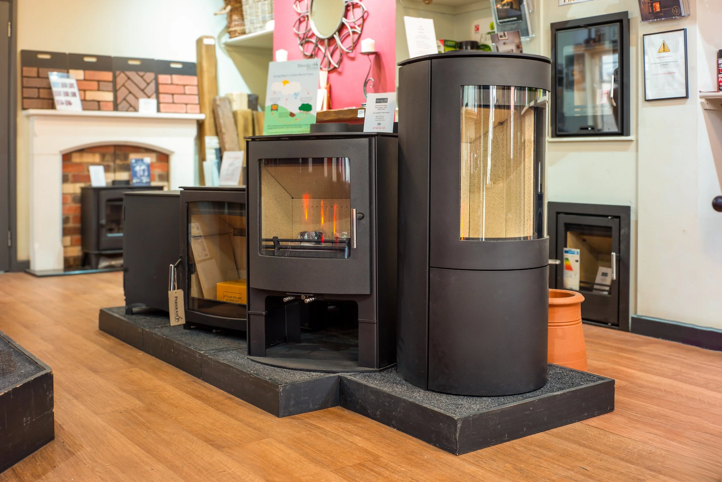 A display of various black electric and gas fireplaces in a showroom, with brick and framed decor on the walls.