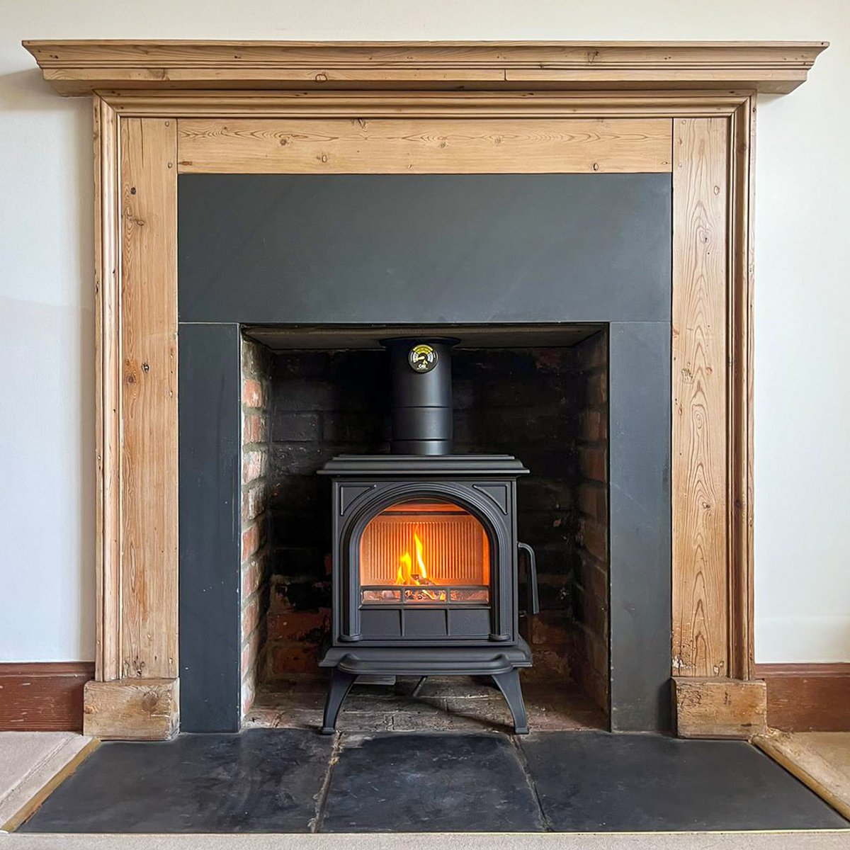 Wood-framed fireplace with a black cast-iron stove, burning fire, set against brick and slate surround.
