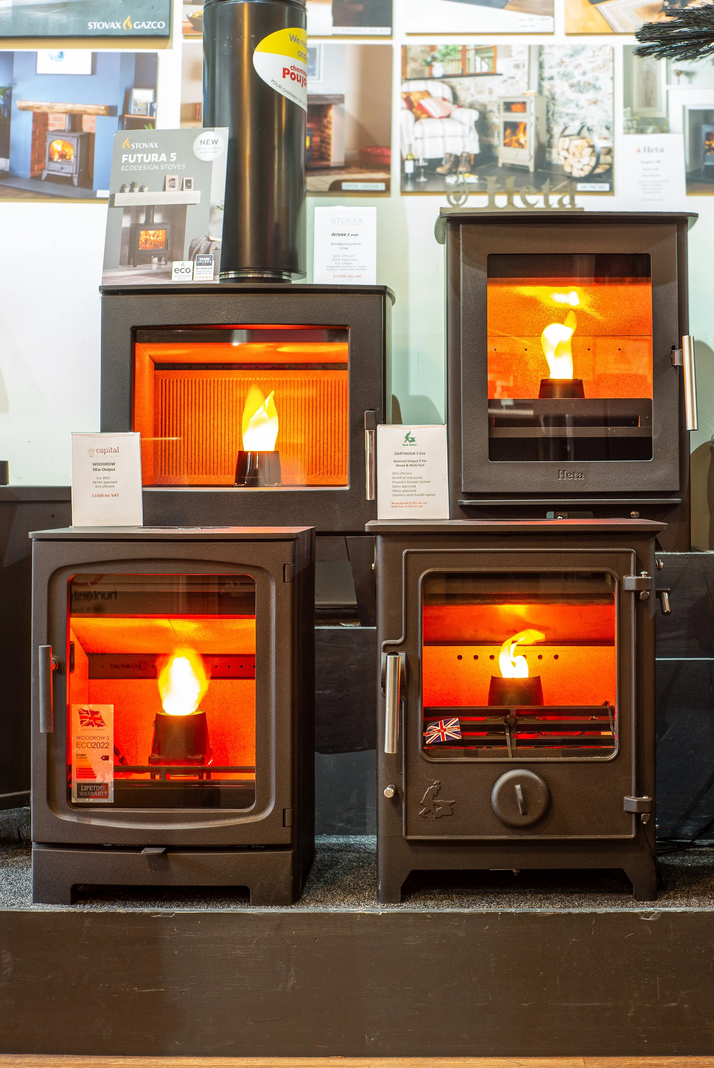 Multiple wood-burning stoves on display in a store, each with visible flames inside.