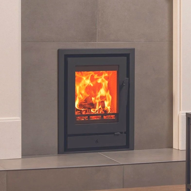 A modern fireplace with a glass door, burning with visible flames and logs inside, surrounded by gray tiles.