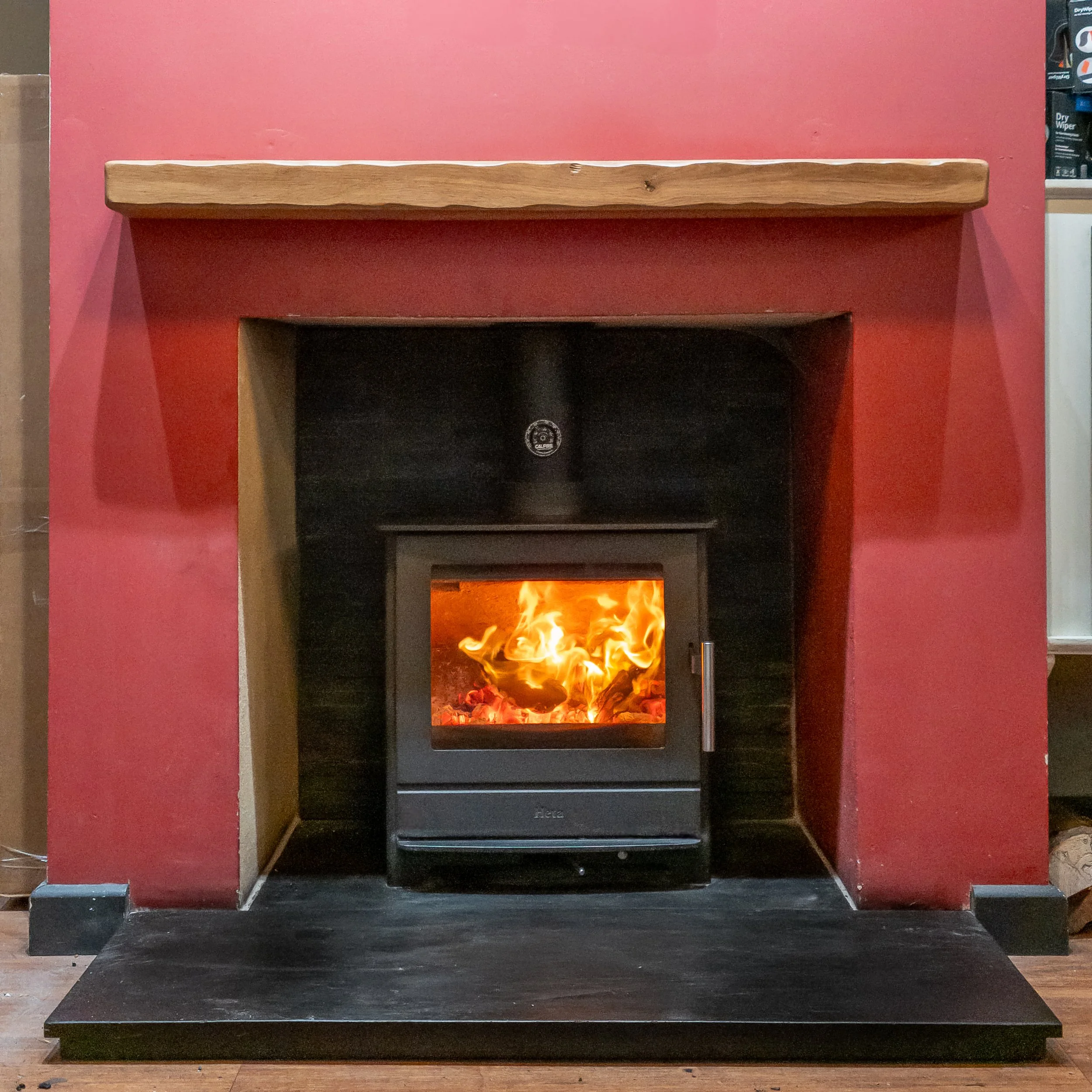 A fireplace with a wooden mantel and a black stove burning with flames.