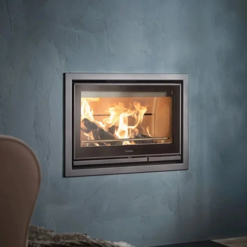 A modern fireplace with glass doors built into a blue textured wall, with visible flames and burning logs inside.