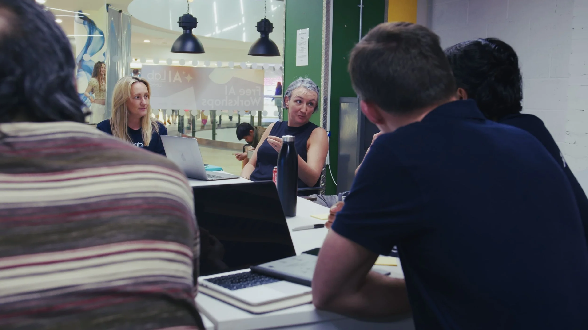 People sitting around a table in a meeting room engaged in a discussion, with laptops and notebooks in front of them.
