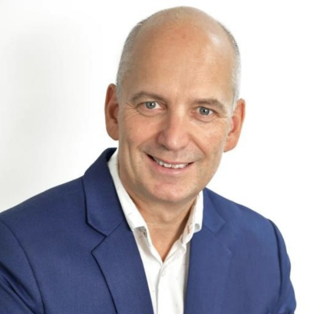 Portrait of a smiling middle-aged man with light skin, short hair, wearing a blue blazer and a white collared shirt, against a white background.
