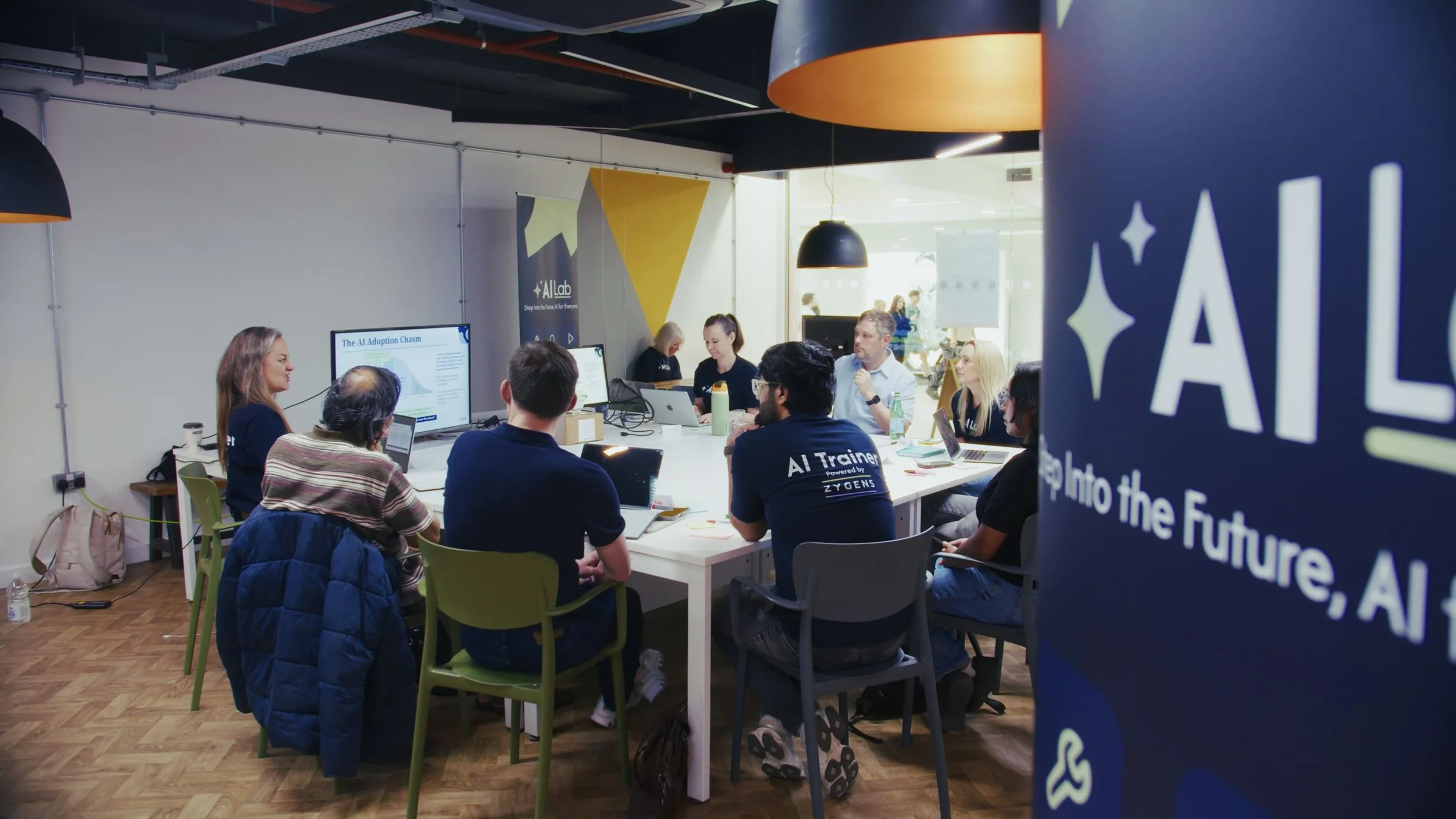 People attending a meeting or workshop in a modern conference room with monitors displaying AI-related content, and banners promoting AI development.