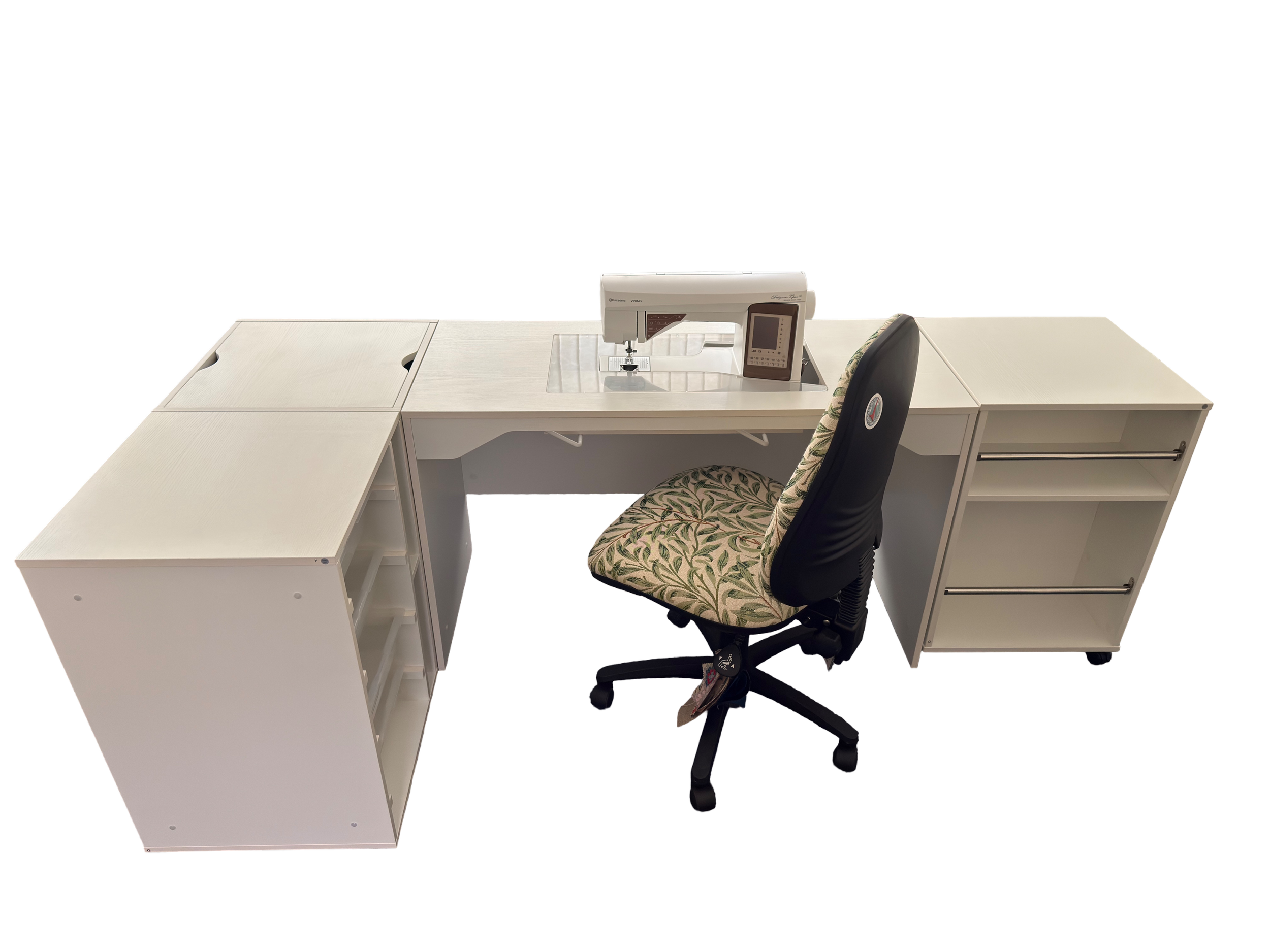 A sewing workspace with a white desk, a sewing machine, a chair with a patterned cushion, and a black office chair, against a solid black background.