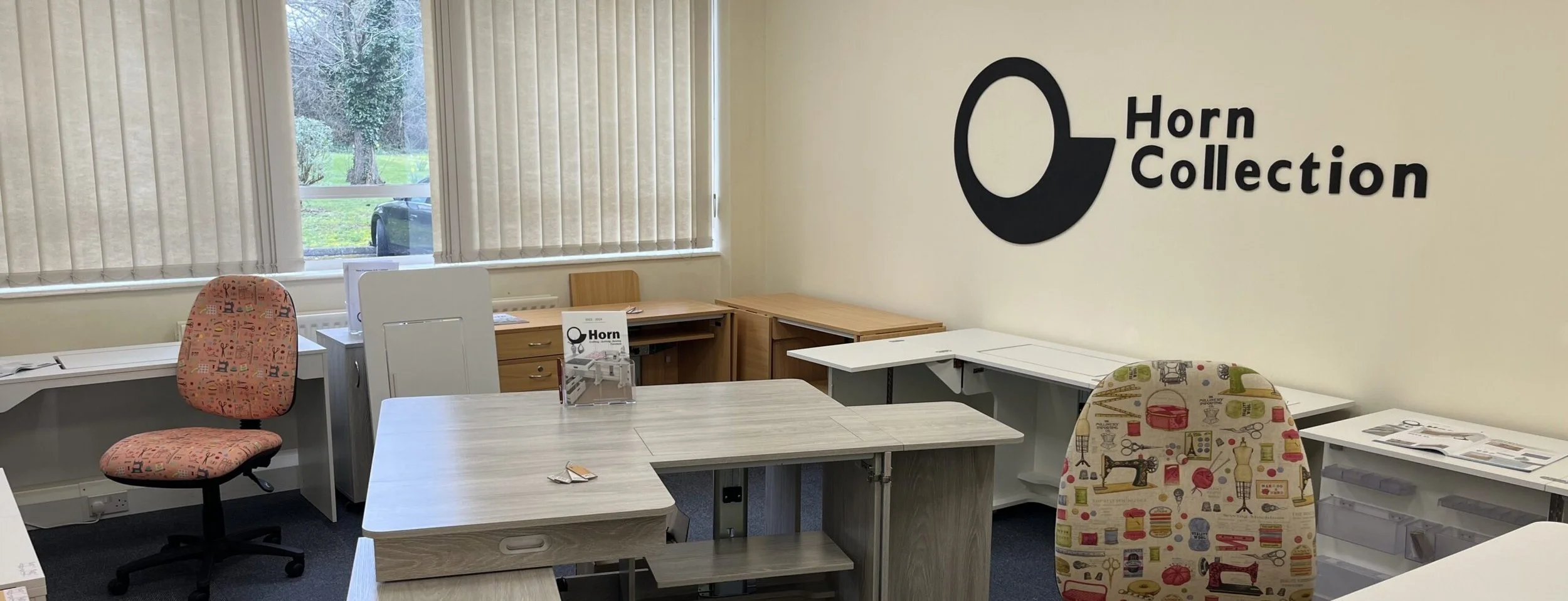 Inside an office with desks, chairs, and a wall decal of a black flower with the words 'Horn Collection'.