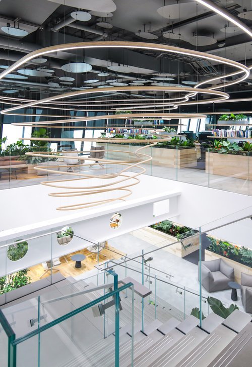 Modern office interior with spiral-shaped hanging light fixtures, glass walls, and track lighting.