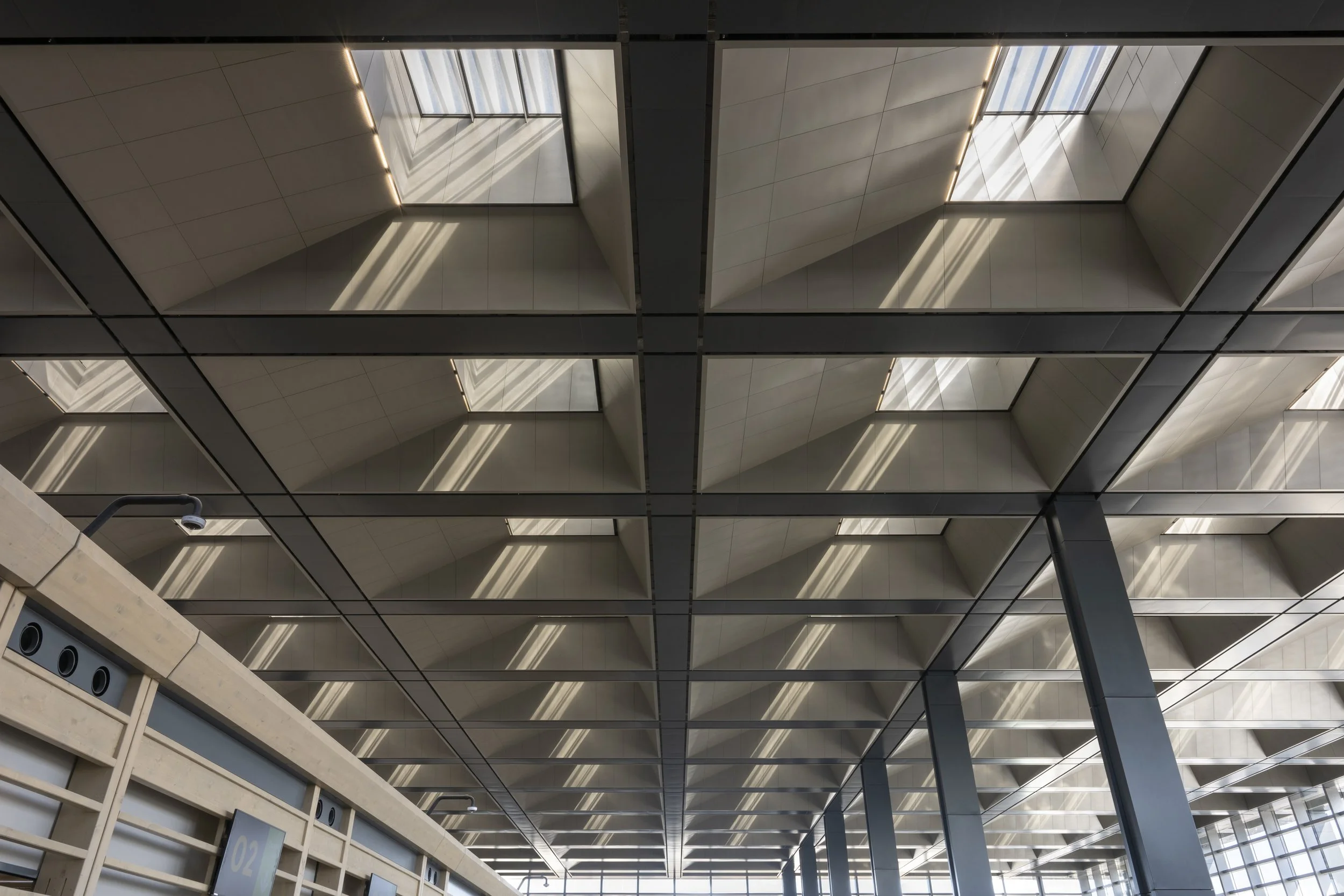 Ceiling of a modern building with large square metal panels and skylights letting in natural light.