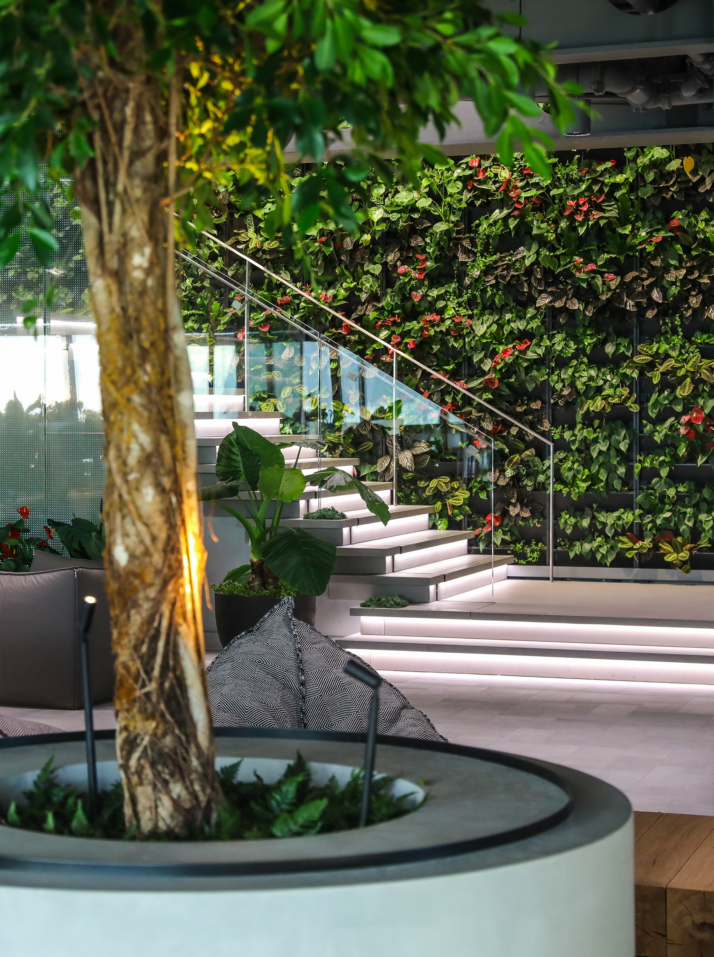 Modern interior space with a staircase, lush green plants, a vertical garden wall, and soft lighting.