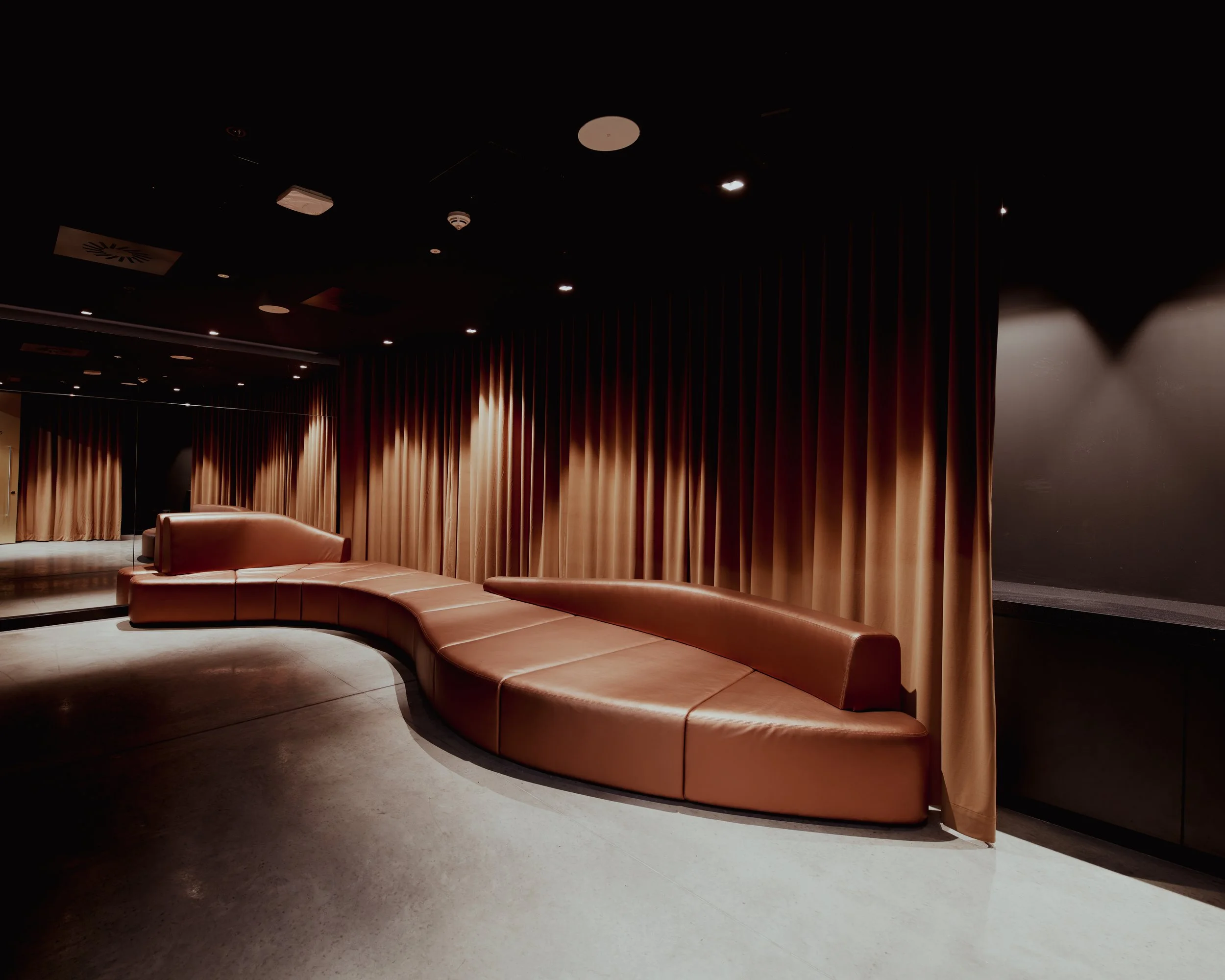 An empty, dimly lit lounge with curved leather seating and brown curtains along the walls.