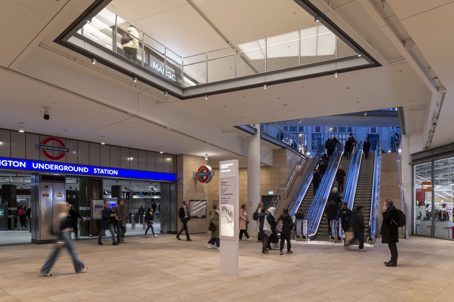 Inside Wembley Underground Station with people walking, escalators, and signage for the station.