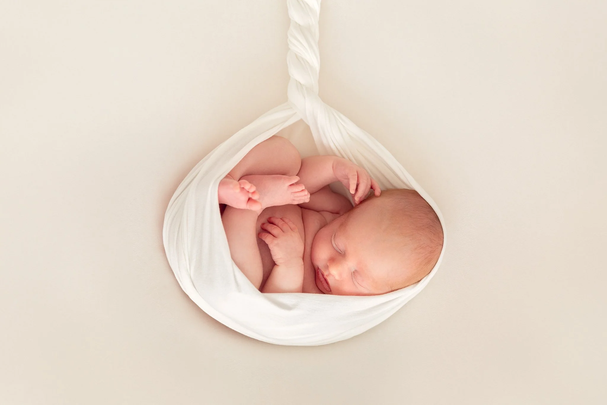 Sleeping newborn baby wrapped in white cloth on a cream-coloured blanket.