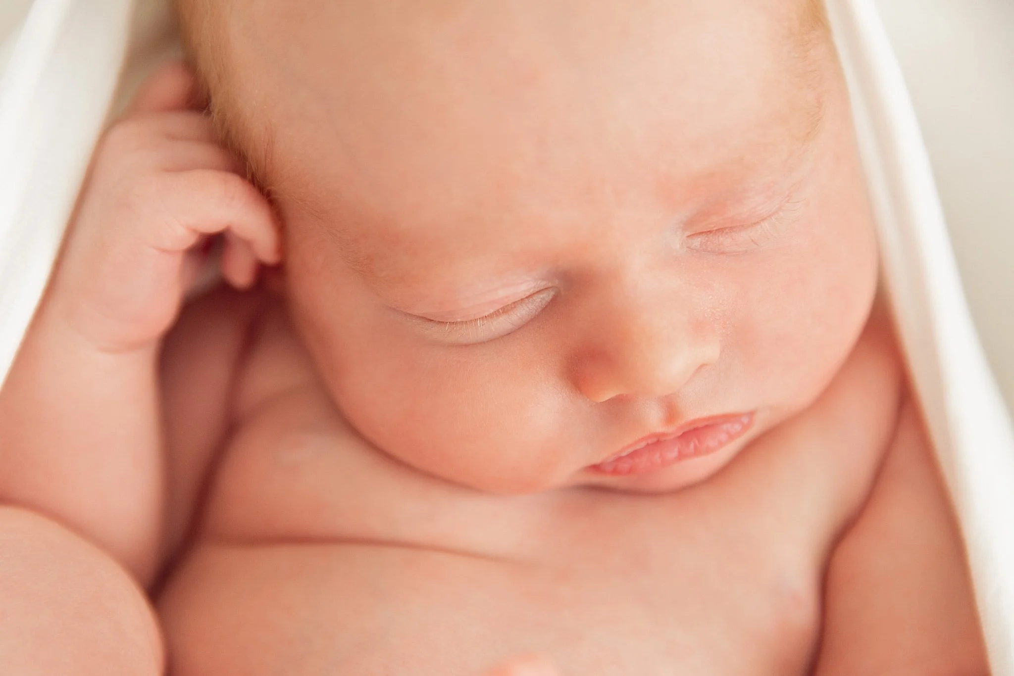 Close-up of a sleeping newborn baby with closed eyes, soft skin, and a relaxed expression.