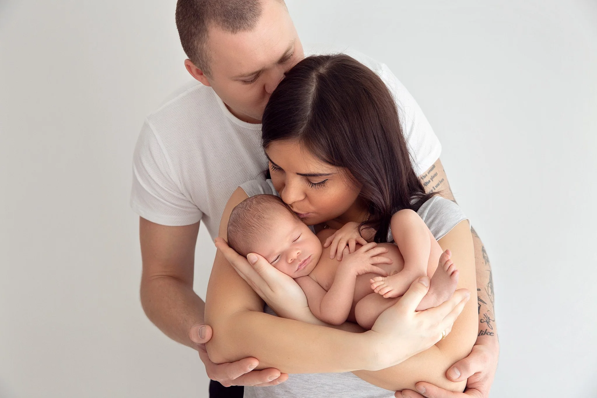 A young family with a father, mother, and newborn baby, loving and holding the baby.