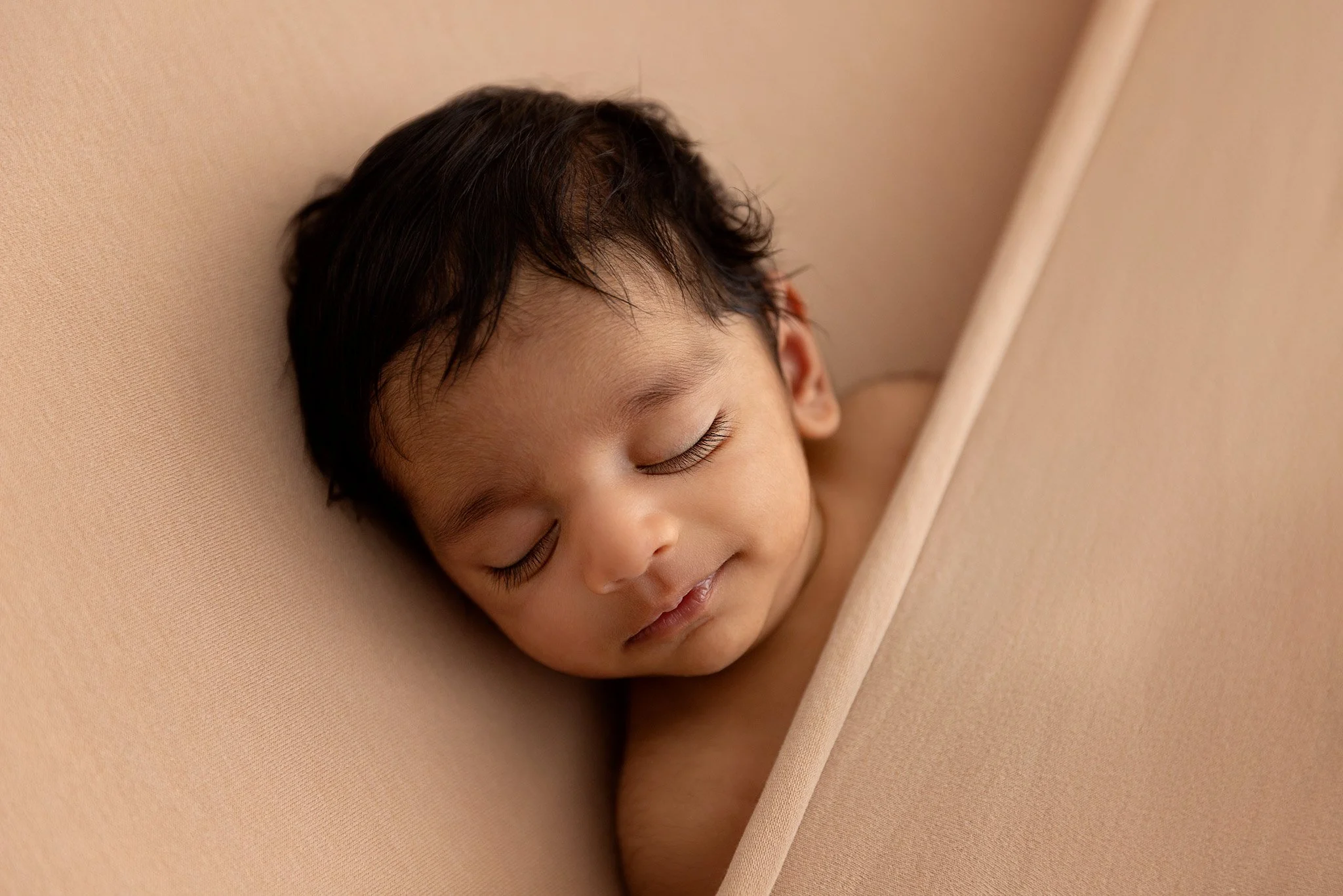 A young boy with dark hair sleeping peacefully on a beige blanket.