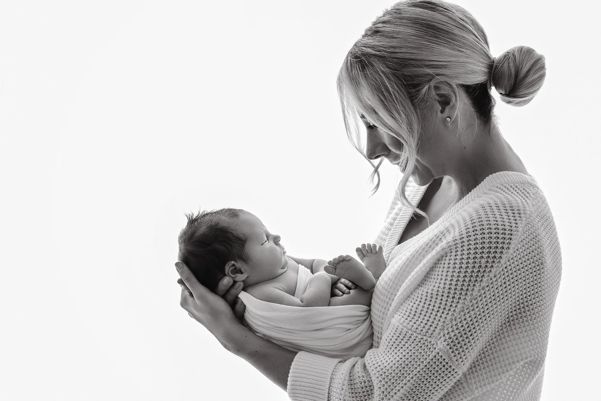 A woman holding a sleeping baby wrapped in a blanket with a plain white background.