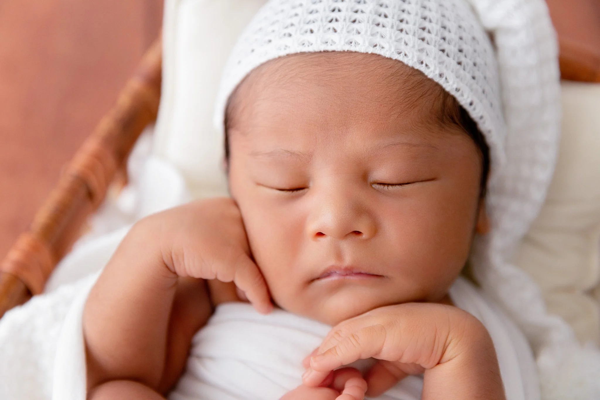 Close-up of a sleeping baby resting on a hand with a white knit cap.