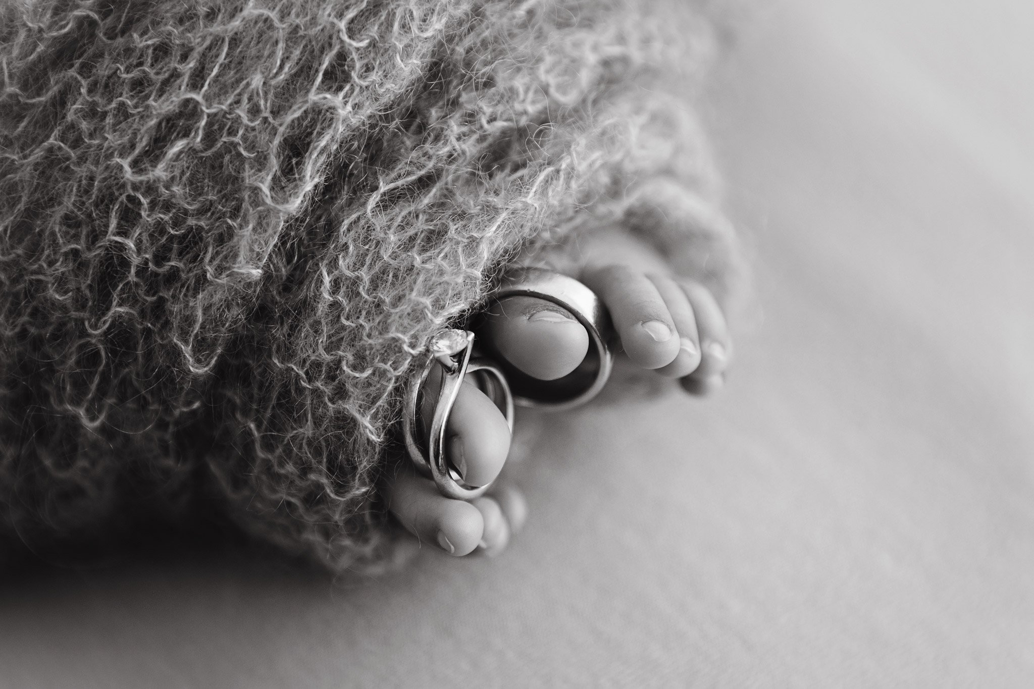 Close-up of baby toes with rings, partly covered by curly textured fabric, resting on a blanket in black and white.