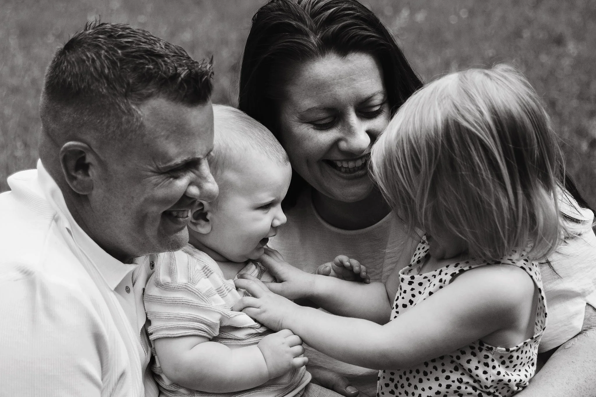 A family of four, including two children, is smiling and playing together outdoors.
