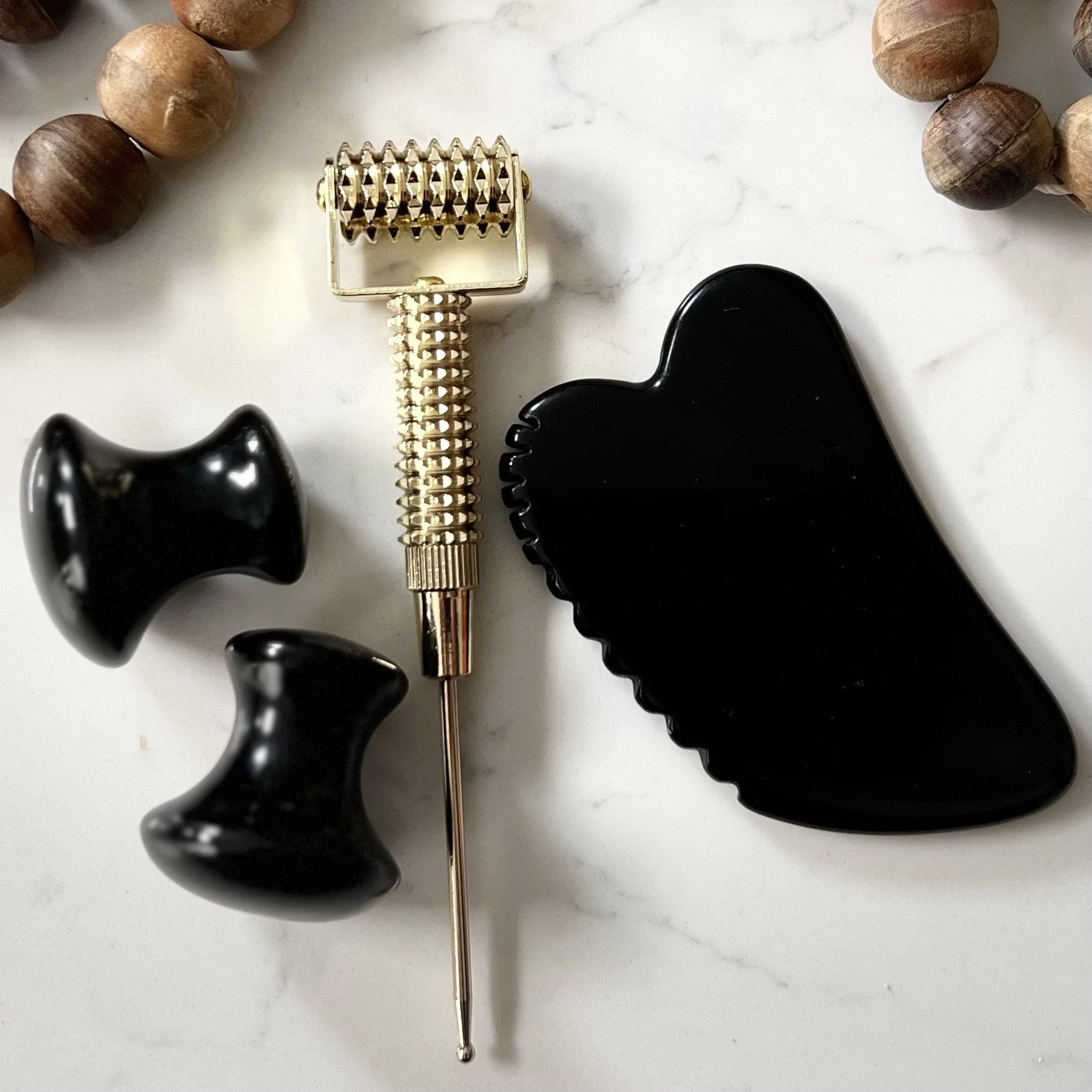 A box of beauty tools including a gold ear piercing tool, two black clips, a black paddle-shaped tool, and a wooden beaded necklace.