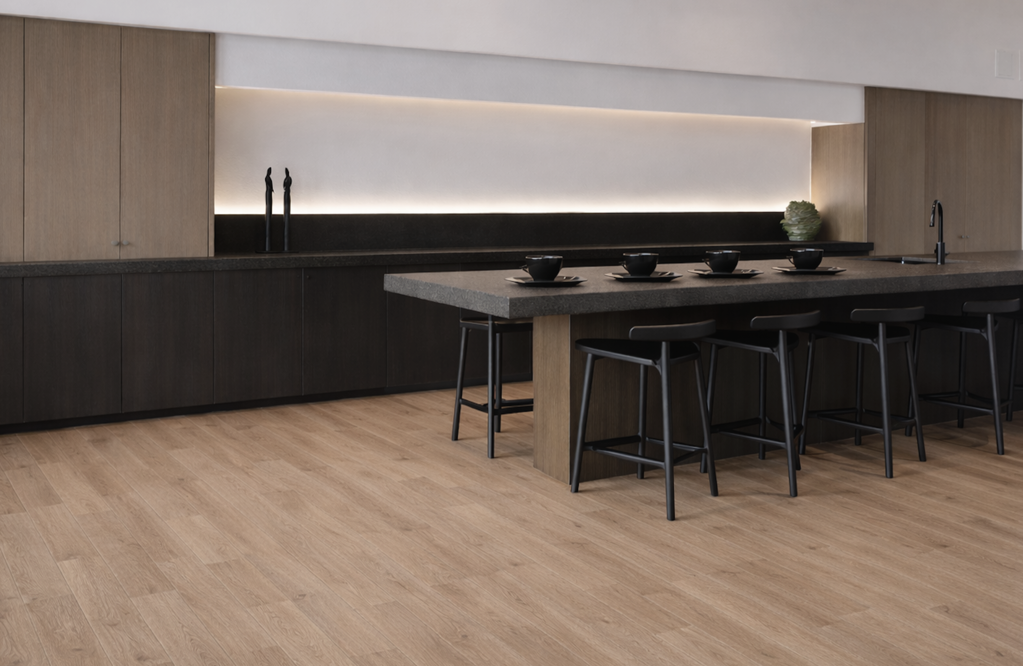 Modern kitchen with light wood flooring, black and beige cabinetry, a dark countertop, a kitchen island with black chairs, black bowls with plates on the island, black kitchen faucet, decor items including black vases and a plant, minimalist design.
