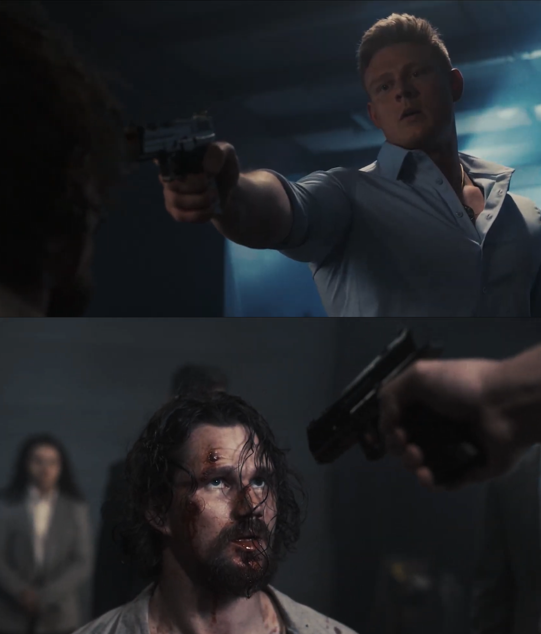 A tense scene of a man in a light-colored shirt pointing a gun at another man with long hair and a beard, who appears injured and bloody, inside a dark room.