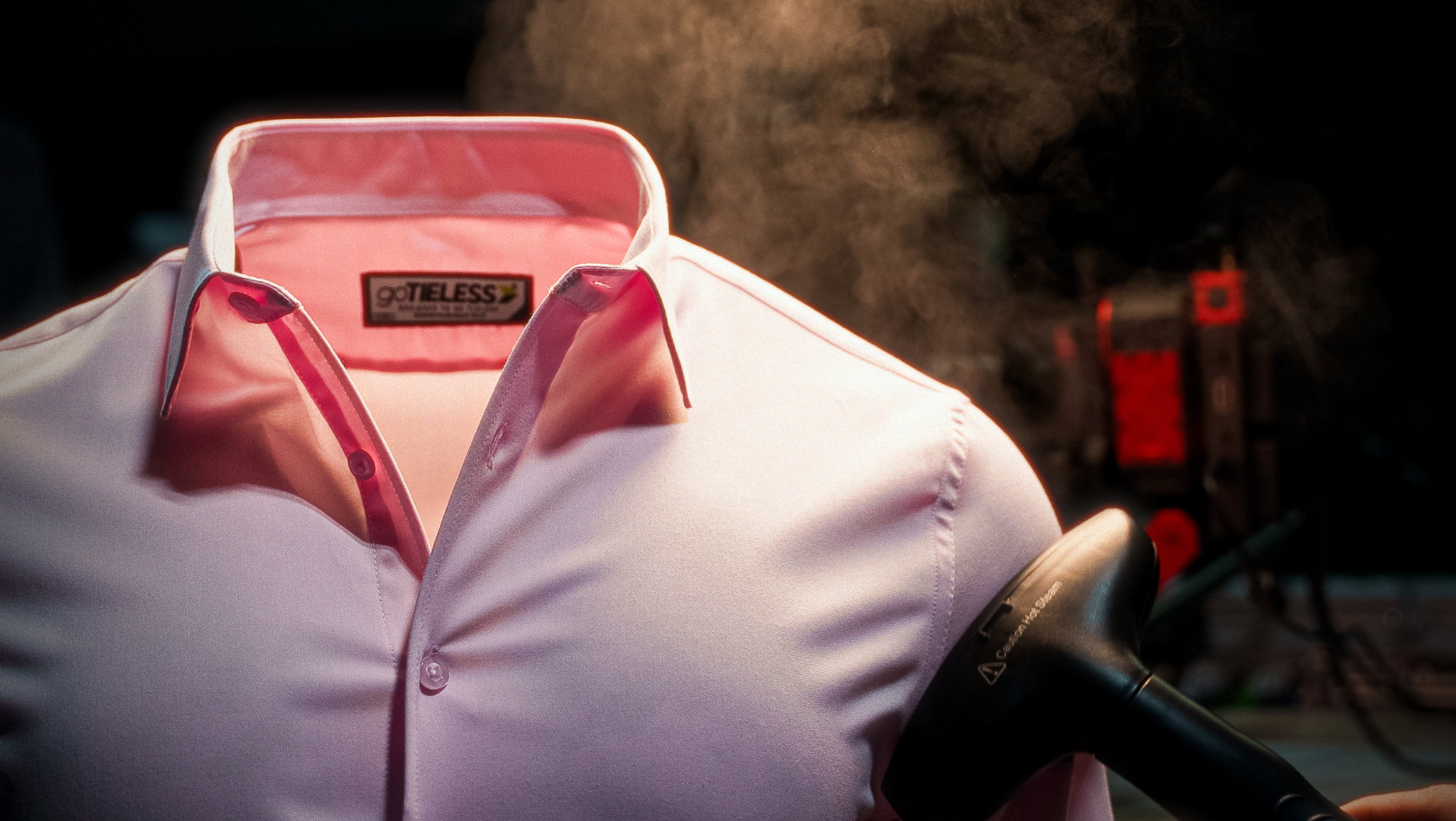 A white dress shirt with pink accents, hanging on a mannequin, with a blow dryer held near the collar.