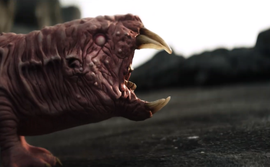 Close-up of a mythical or fictional creature with a wrinkled, pinkish skin, sharp teeth, and small eyes, on a dark surface with a blurred background.