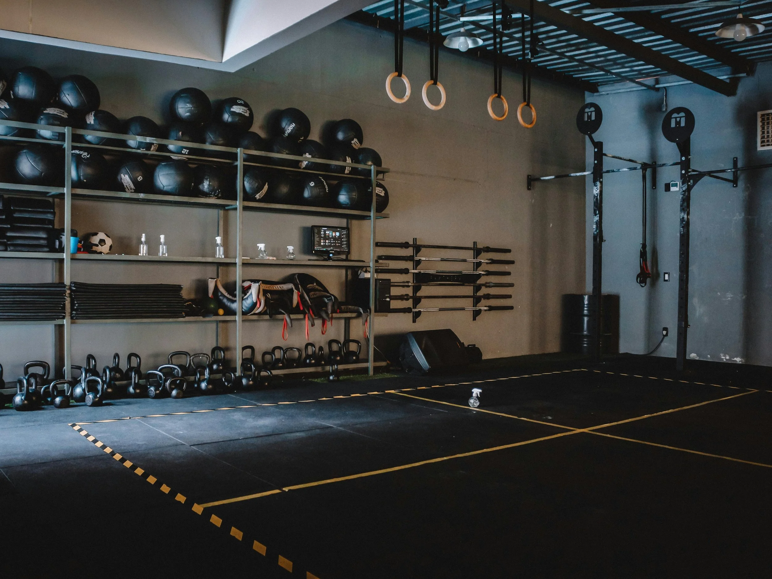 Ein leeres Fitnessstudio mit schwarzen Gymnastikmatten, Hanteln, Kugelhanteln, Medizinbällen und Turnringen.– Personal Training Schweiz