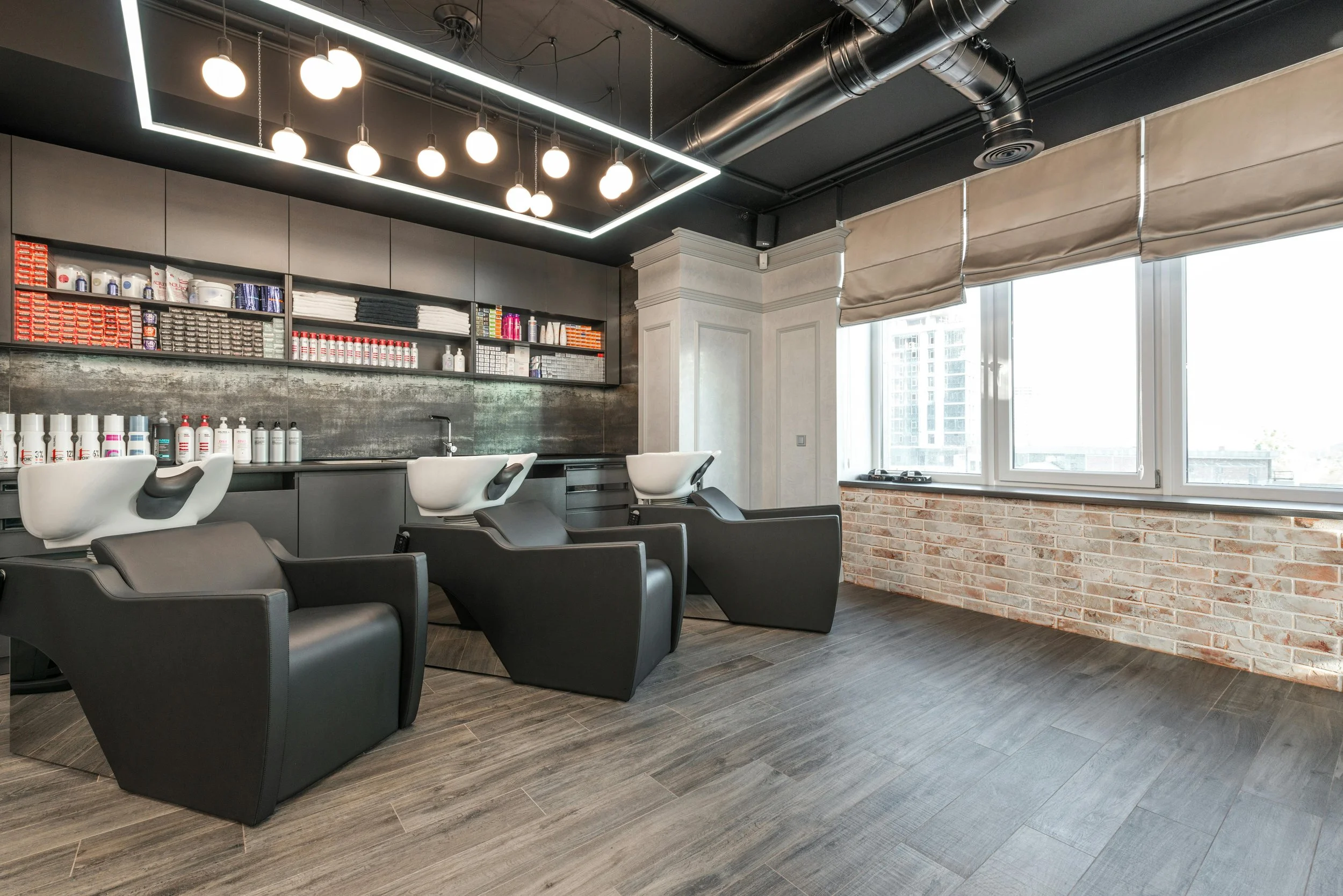 Ein moderner Friseursalon mit schwarzen Liegesesseln und Waschbecken, Regalen mit Haarpflegeprodukten, großen Fenstern und industriellem Design.– Coiffeur Schweiz