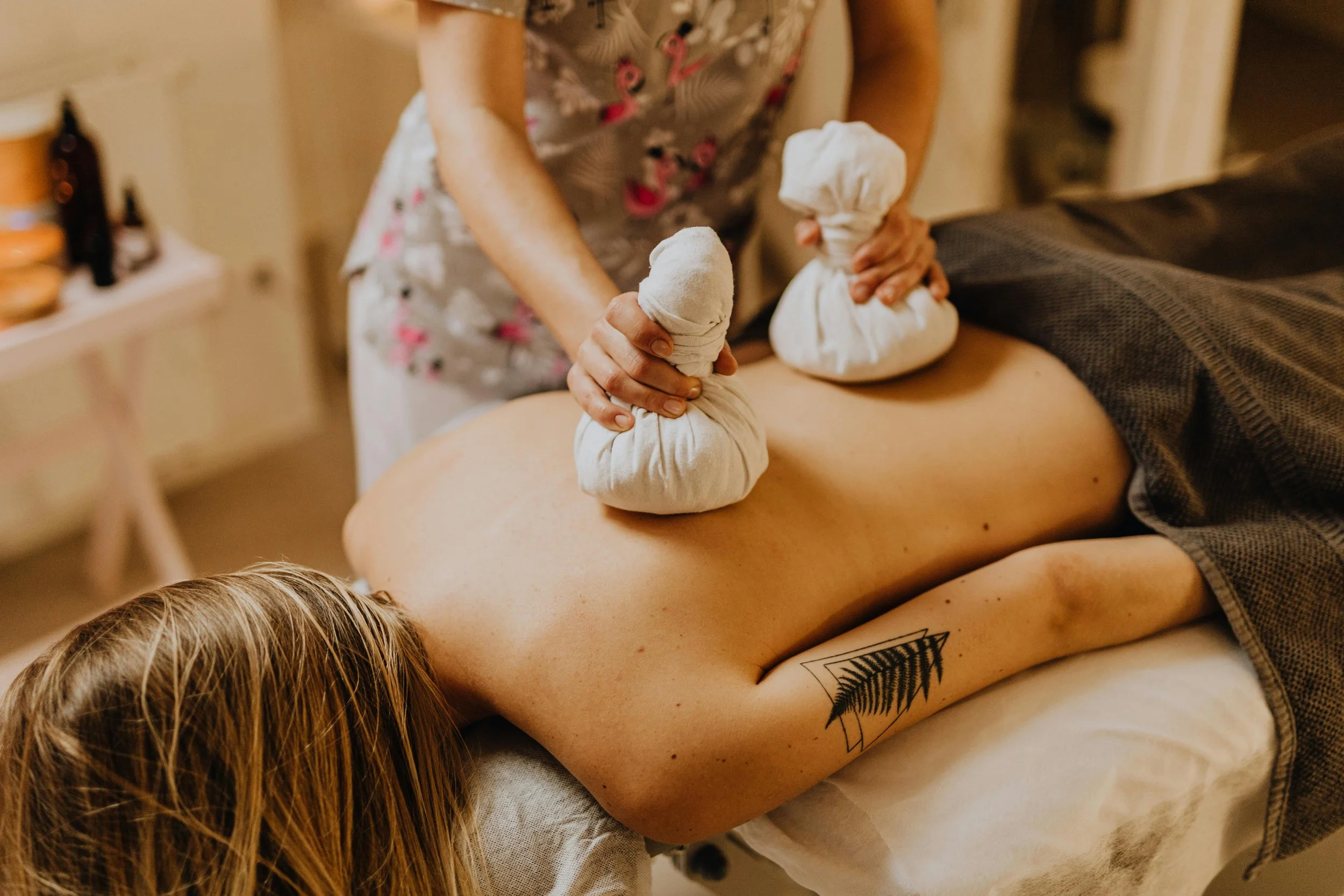 Person erhält eine Massage mit warmen Kräuterstrümpfen auf dem Rücken, während sie auf dem Bauch liegt.– TCM Schweiz