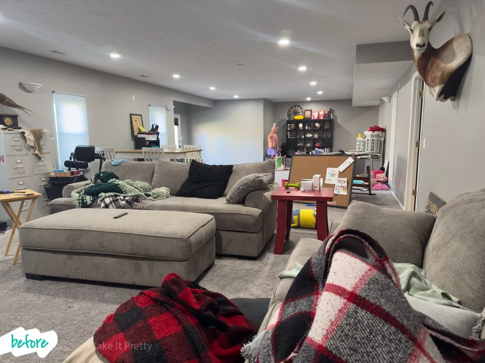 A living room with beige sofas, a red side table, a mounted deer head on the wall, and a play area with toys in the background.
