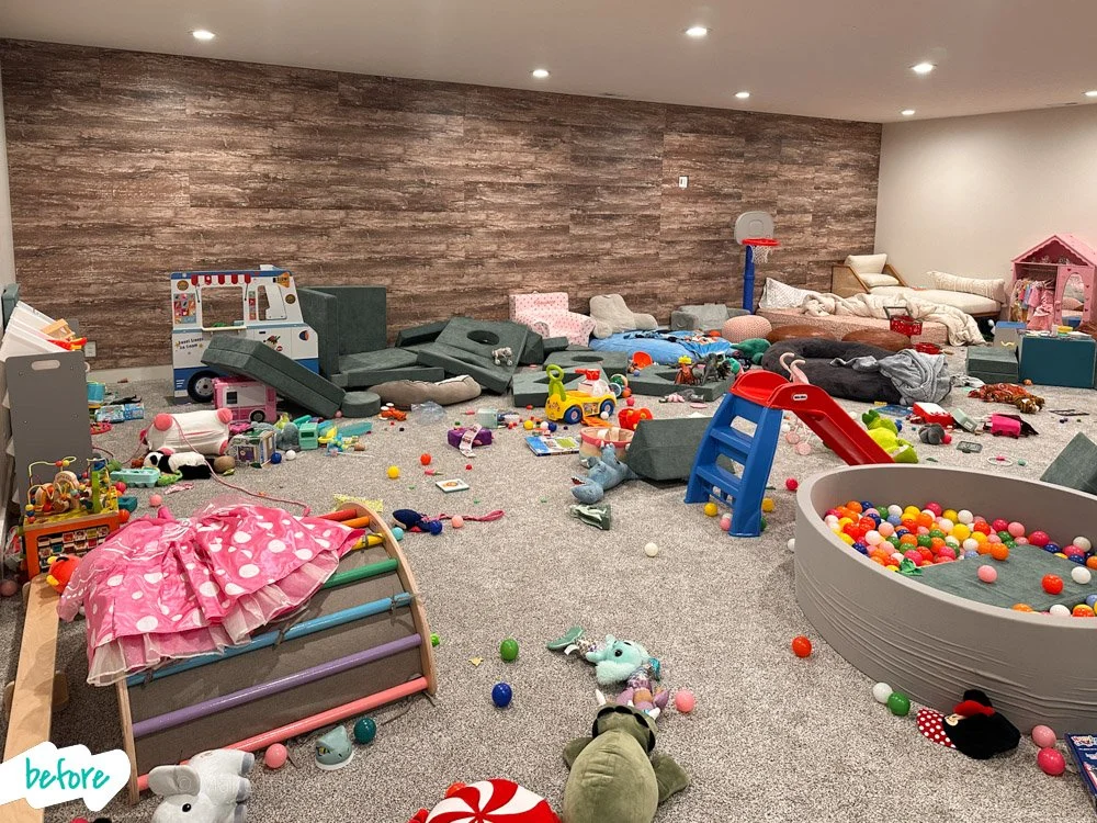 Disorganized playroom with stuffed animals, toys, a ball pit, a slide, beds, and scattered objects on the carpet.