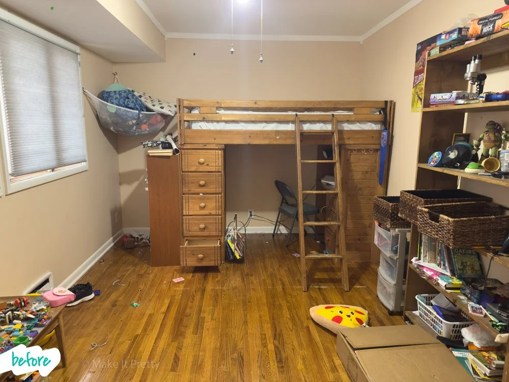 A cluttered bedroom with a wooden loft bed, a ladder, a desk underneath, and a chair. There is a window on the left with closed blinds, a wooden shelf on the right filled with toys and books, and various toys and objects scattered on the floor and sh