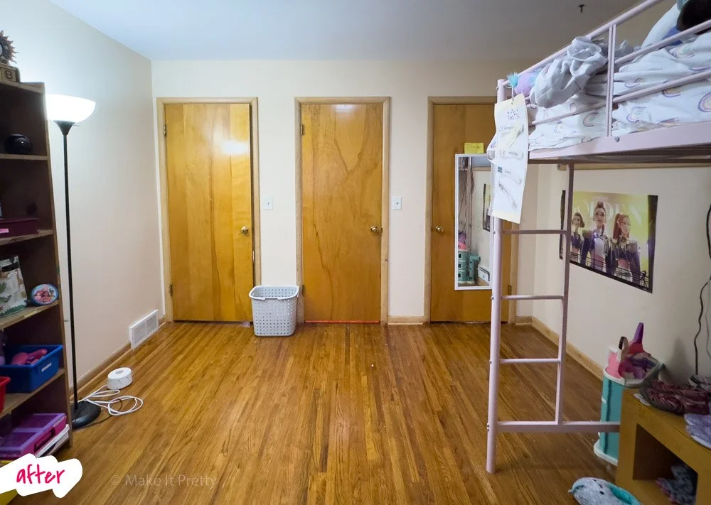 A bedroom with three closed wooden doors, a loft bed with toys and a blanket, a television with children on screen, a bookshelf with children's toys, and a floor lamp.