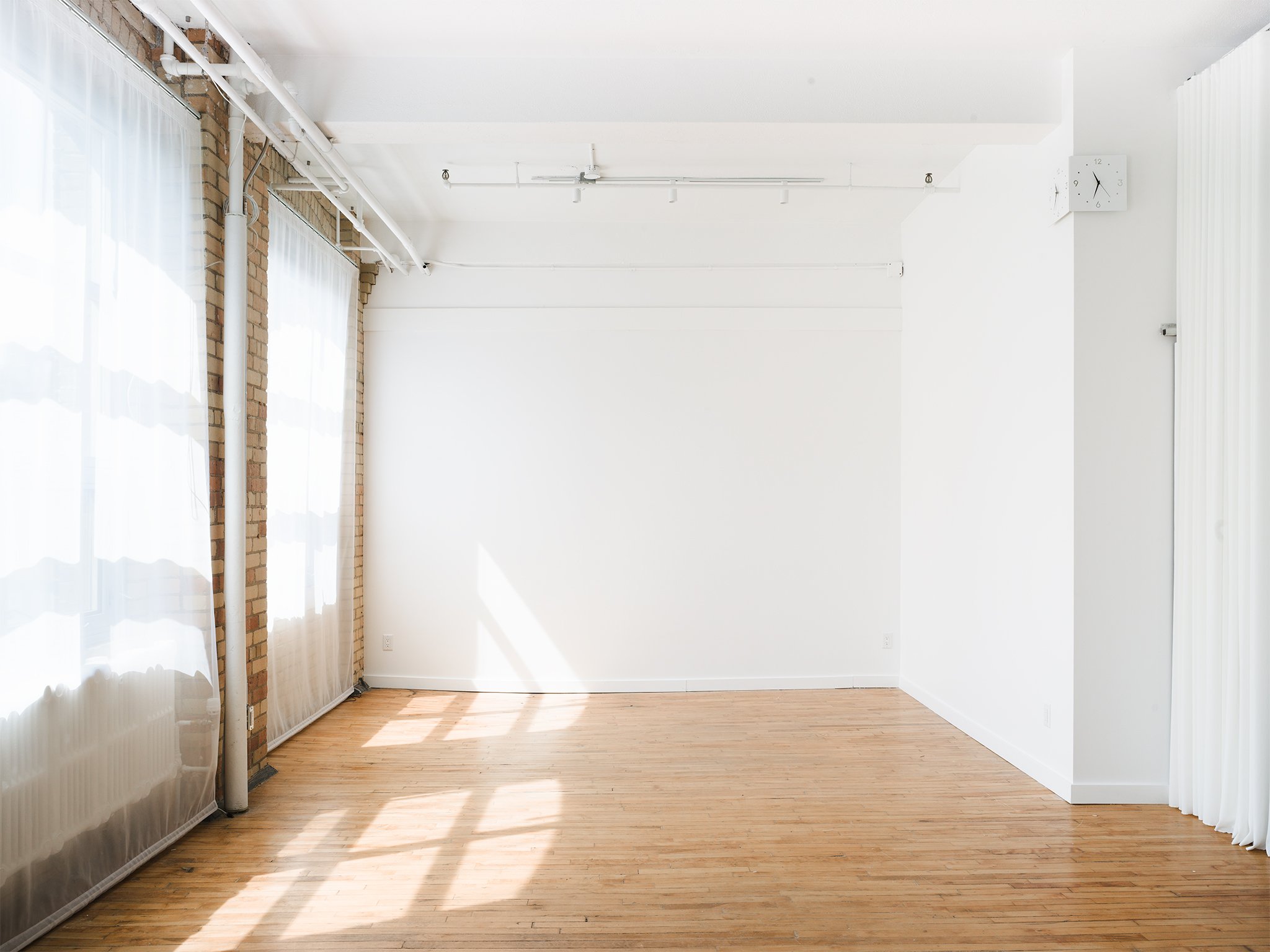Sunlit white wall at On2 Studio in downtown Toronto, an empty natural light photo space with exposed brick and hardwood floors.