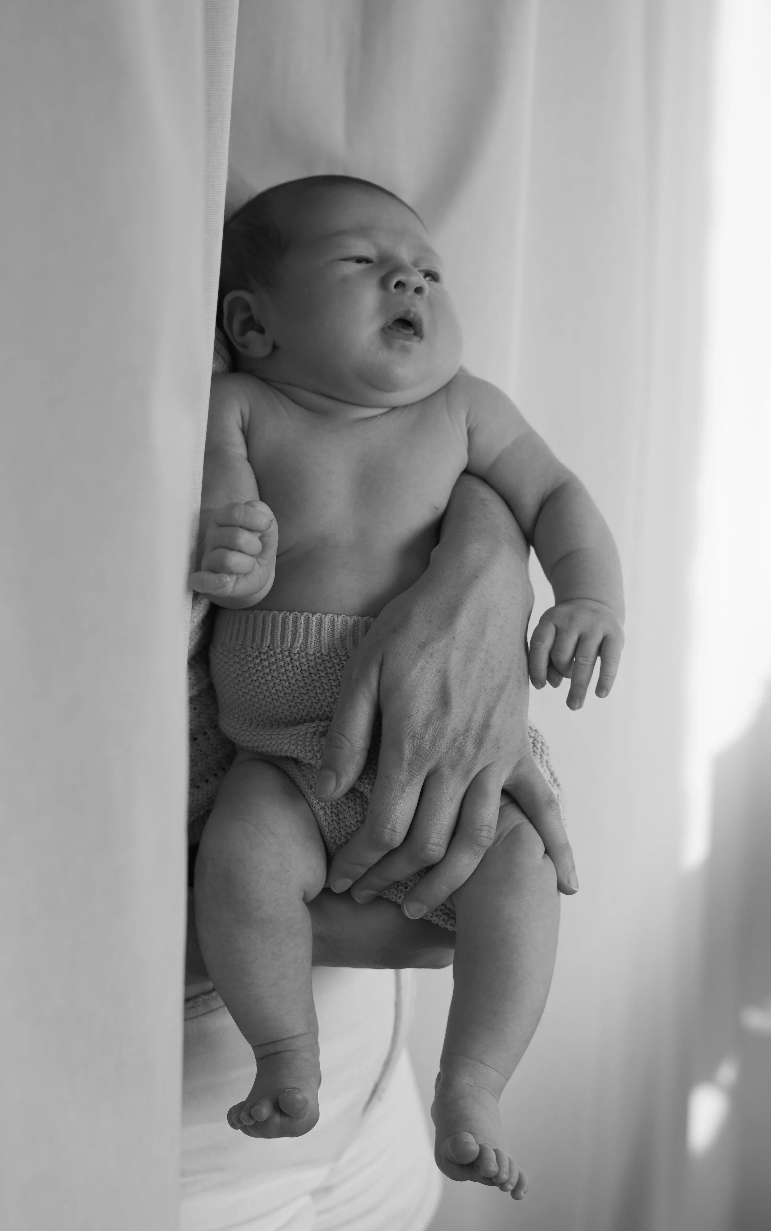 Zwart-wit foto van een pasgeboren baby die in de armen van iemand ligt, die de buik en benen van de baby vasthoudt.