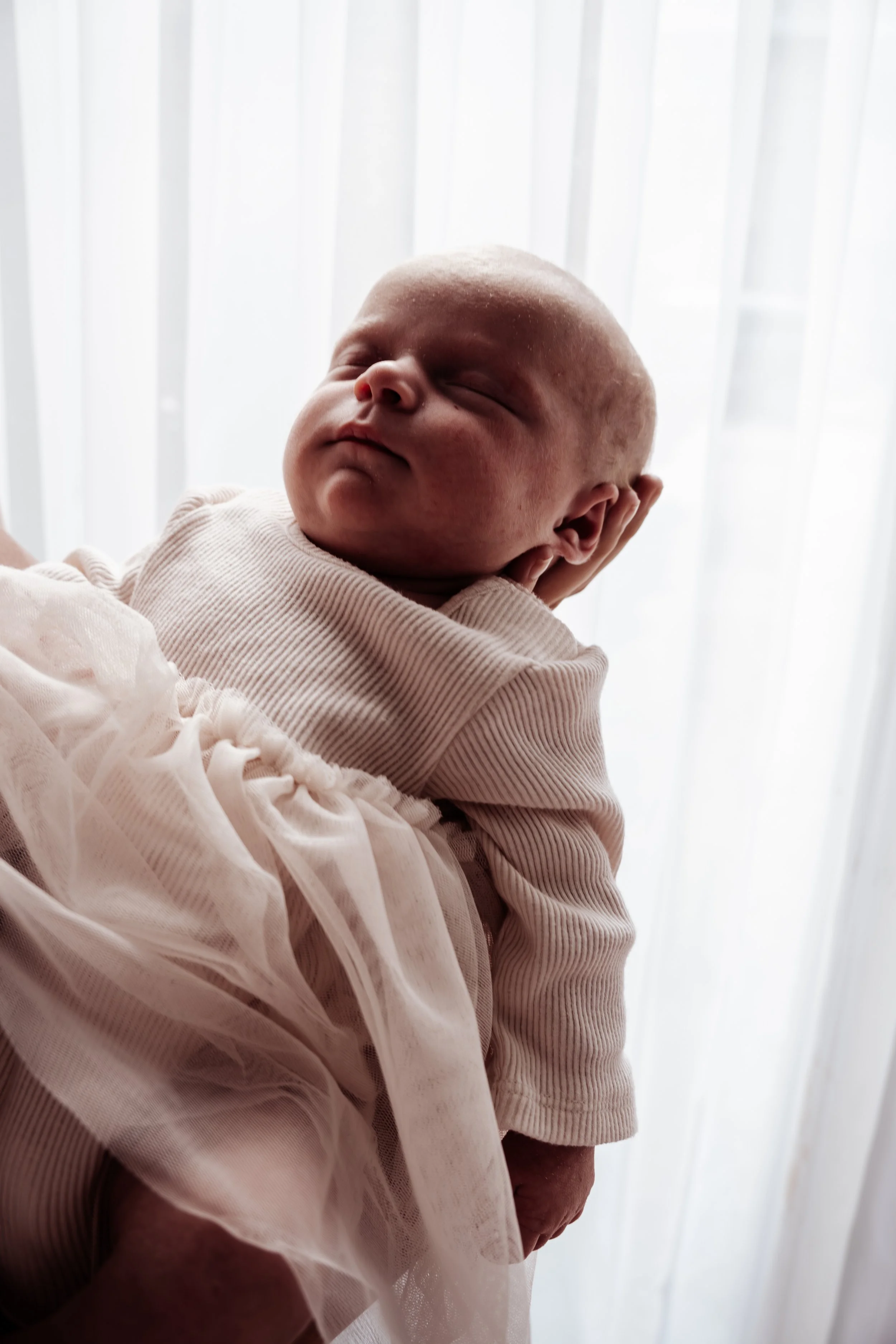 Zachtaardige close-up van slapende baby met lichte huid, gekleed in lichtroze kleding en een tule rok, voor een witte achtergrond.