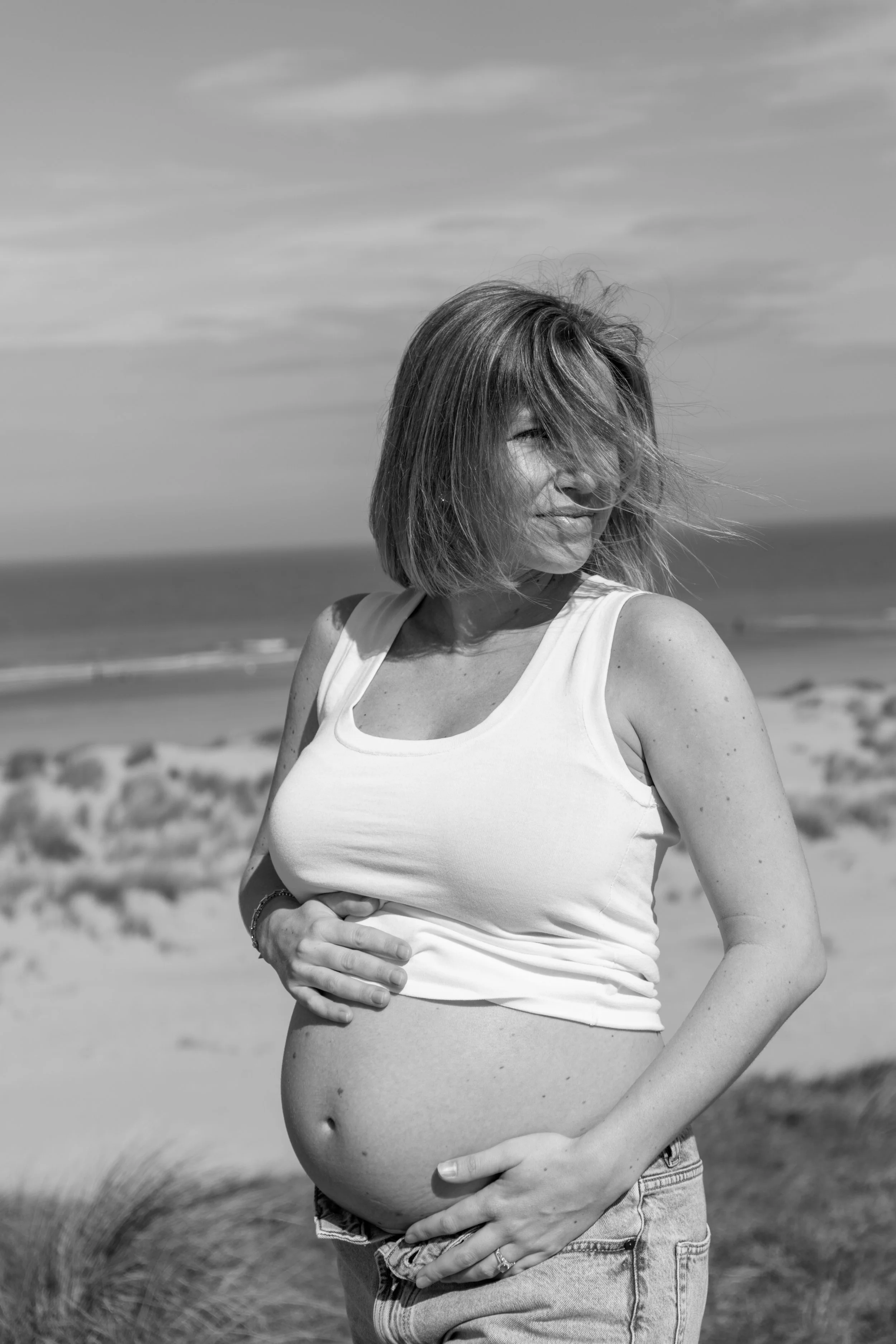 Zwangere vrouw op het strand met wind in haar haar, zwart-wijn.