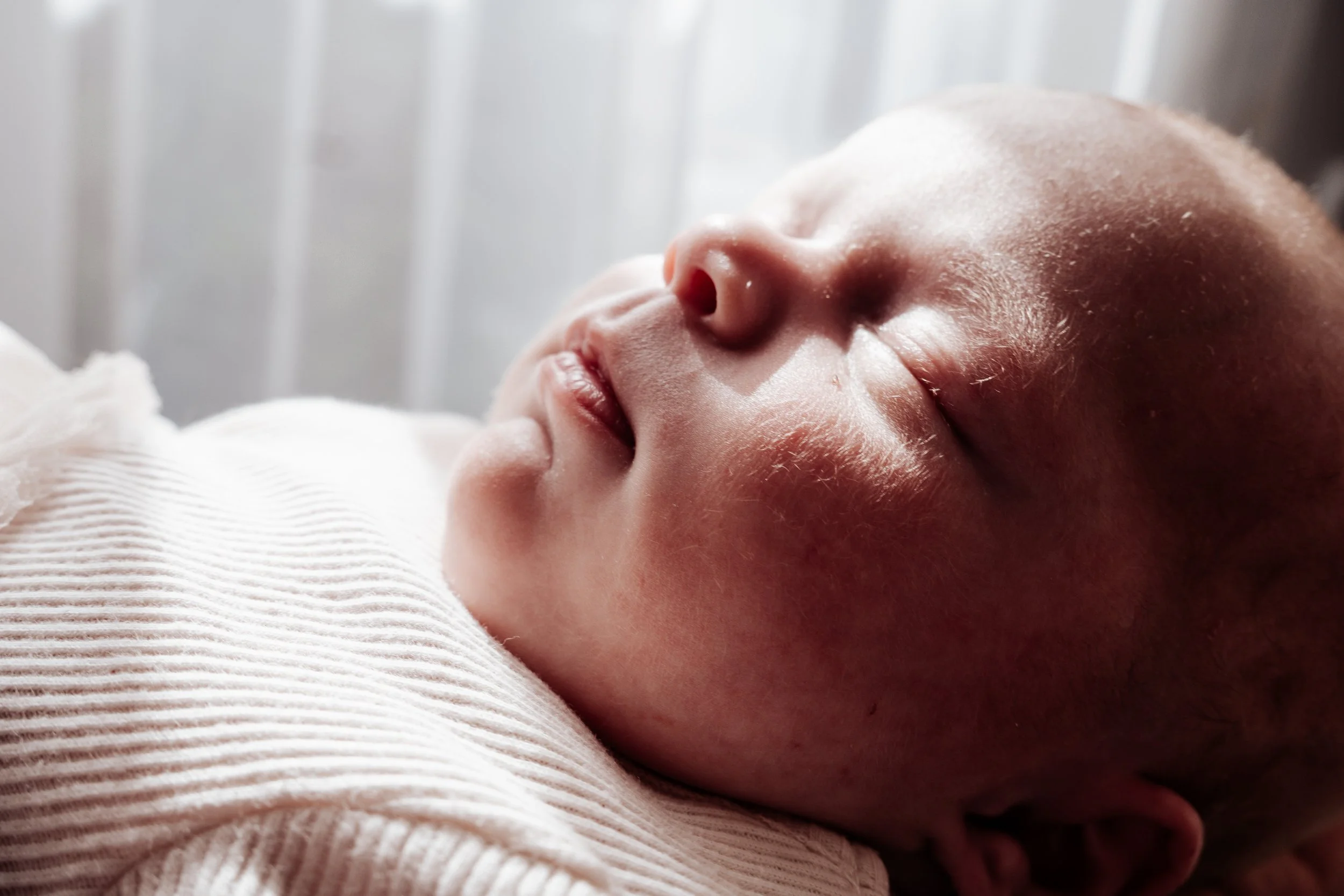 Close-up van een slapende baby met gesloten ogen, liggend op een zachte, gebreide doek, met zacht licht op het gezicht.